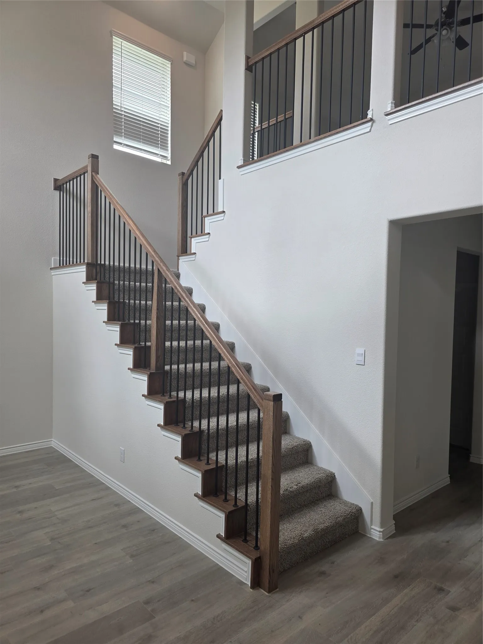 Two-story entryway featuring wood-finish flooring and a carpeted staircase with wood newel posts and black iron balusters