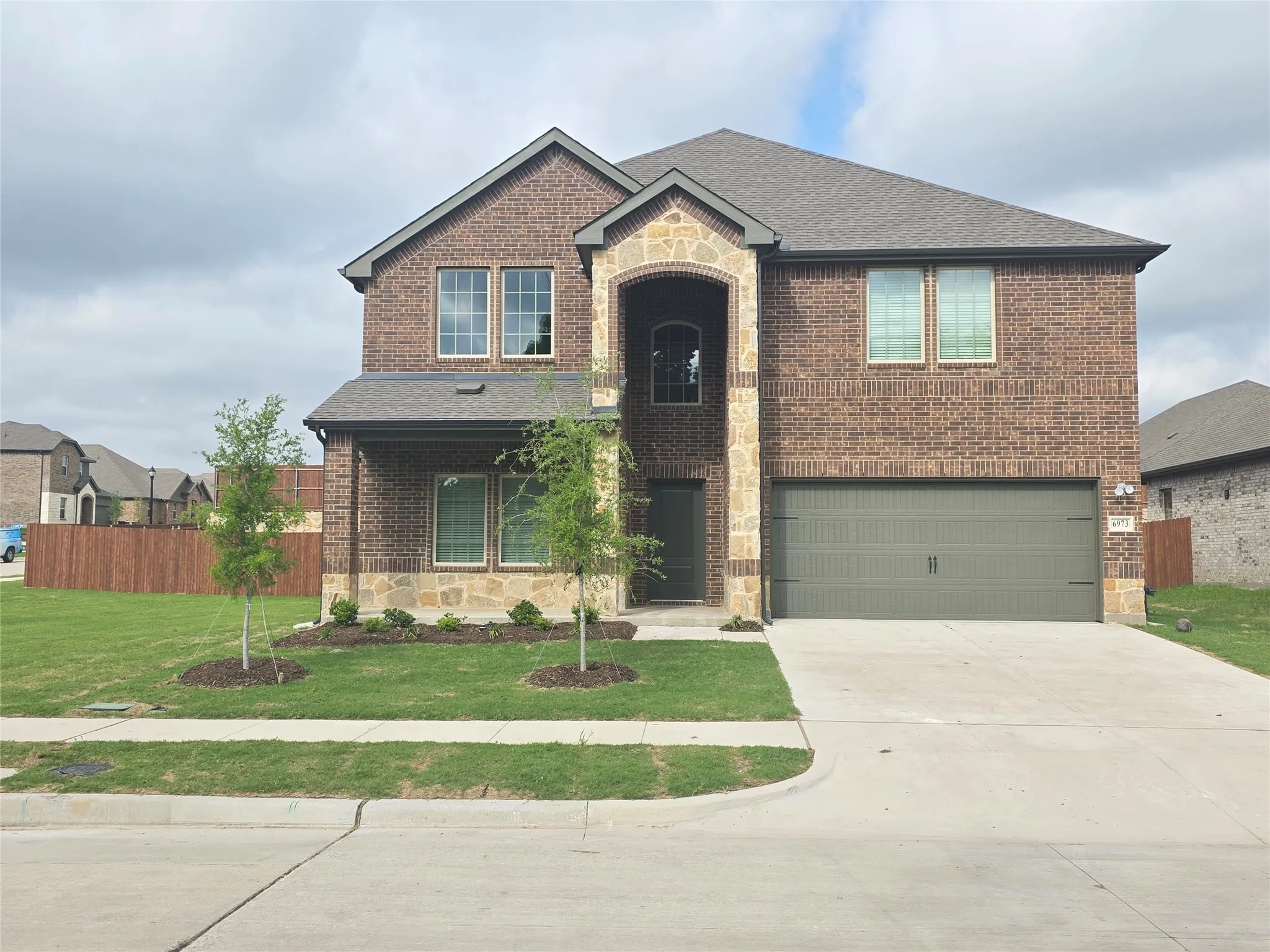 Two-story brick and stone facade residence featuring a covered entry, an arched stone portico, a two-car garage with a panel door, and mature landscaping