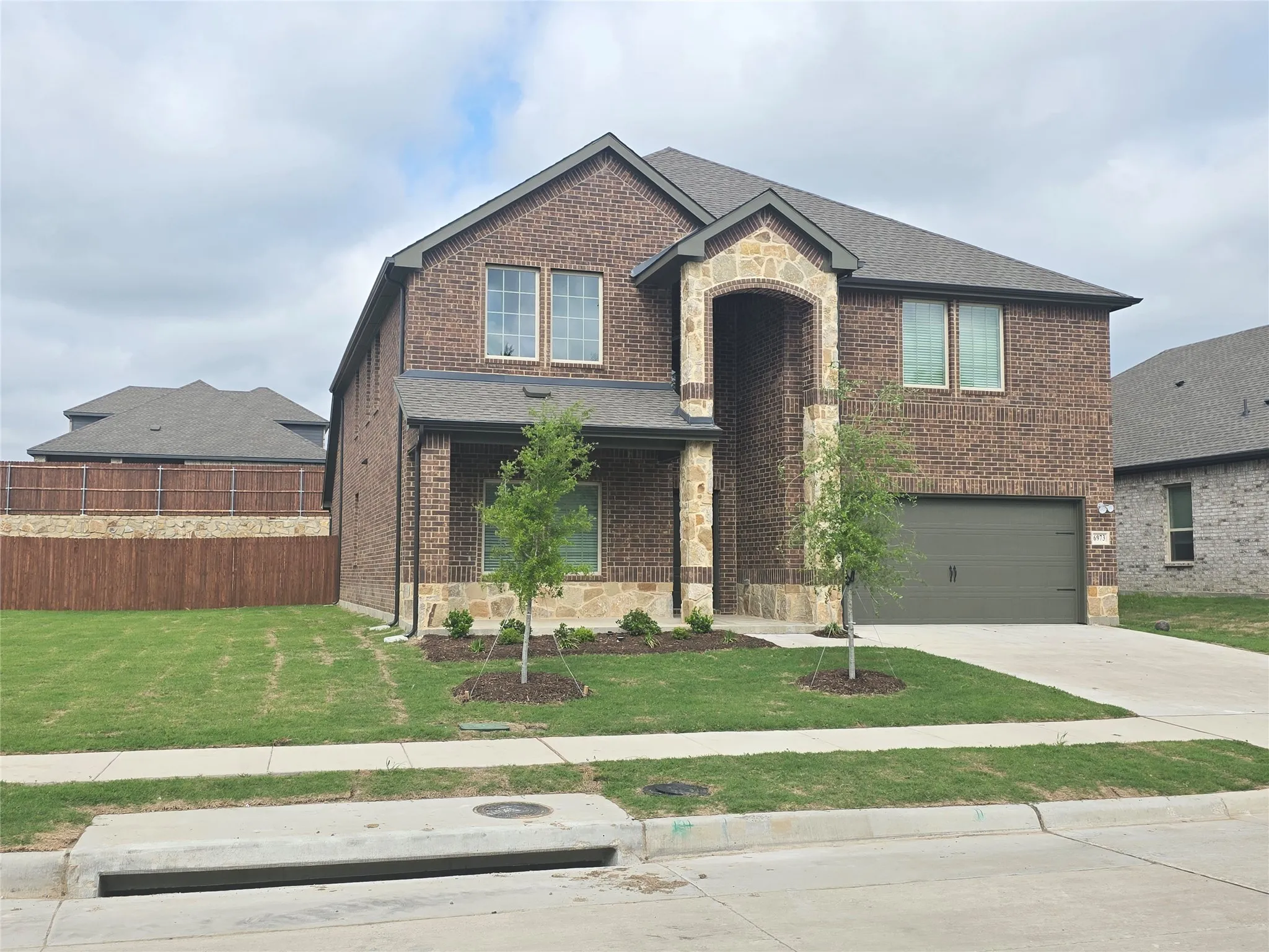 Two-story brick and stone facade residence featuring a covered entry porch, dark gray garage door, and a shingle roof