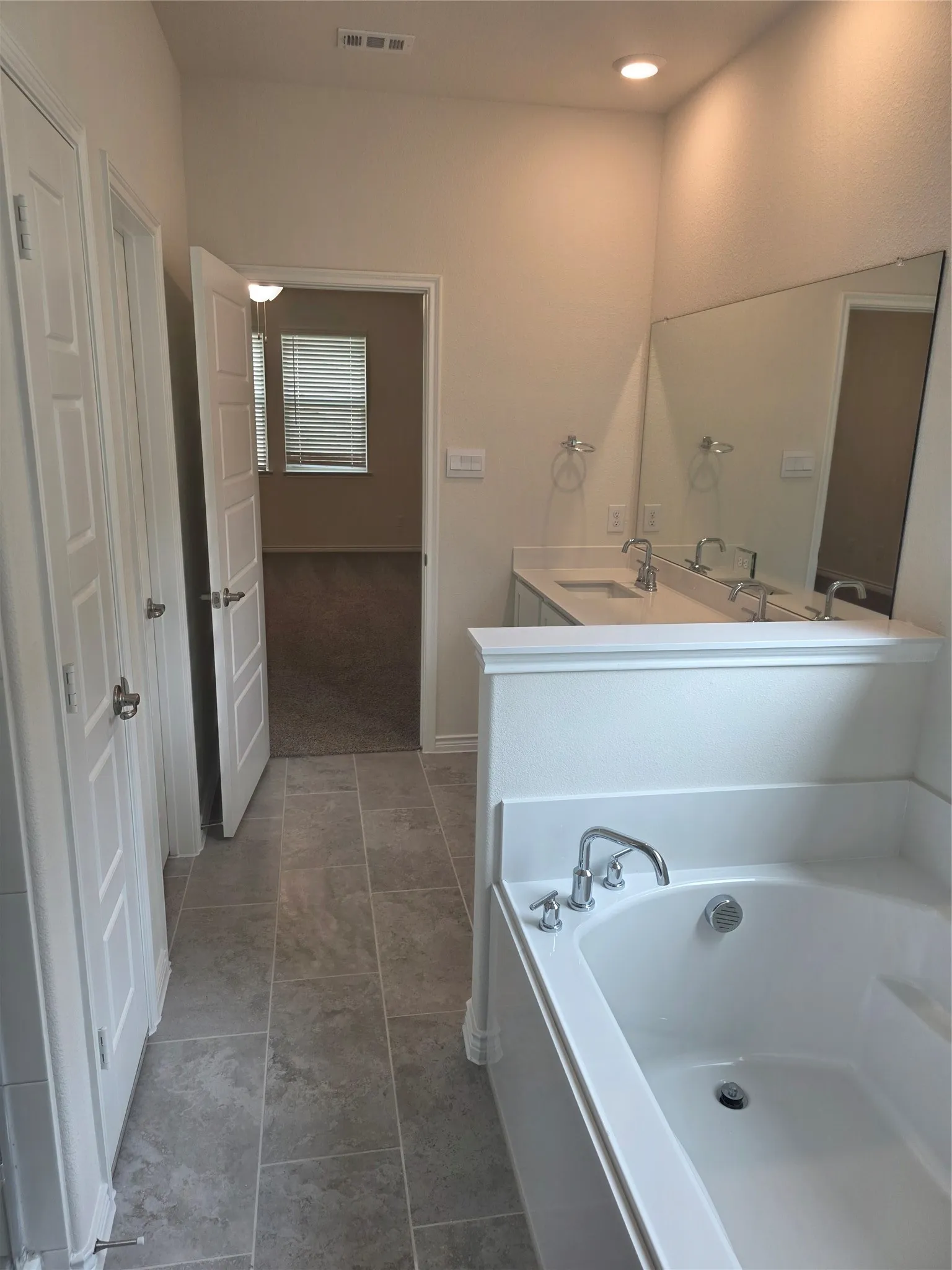 Bathroom featuring a built-in soaking tub with chrome fixtures, dual vanity with undermount sinks and chrome faucets, large wall-mounted mirror, recessed lighting, and tile flooring