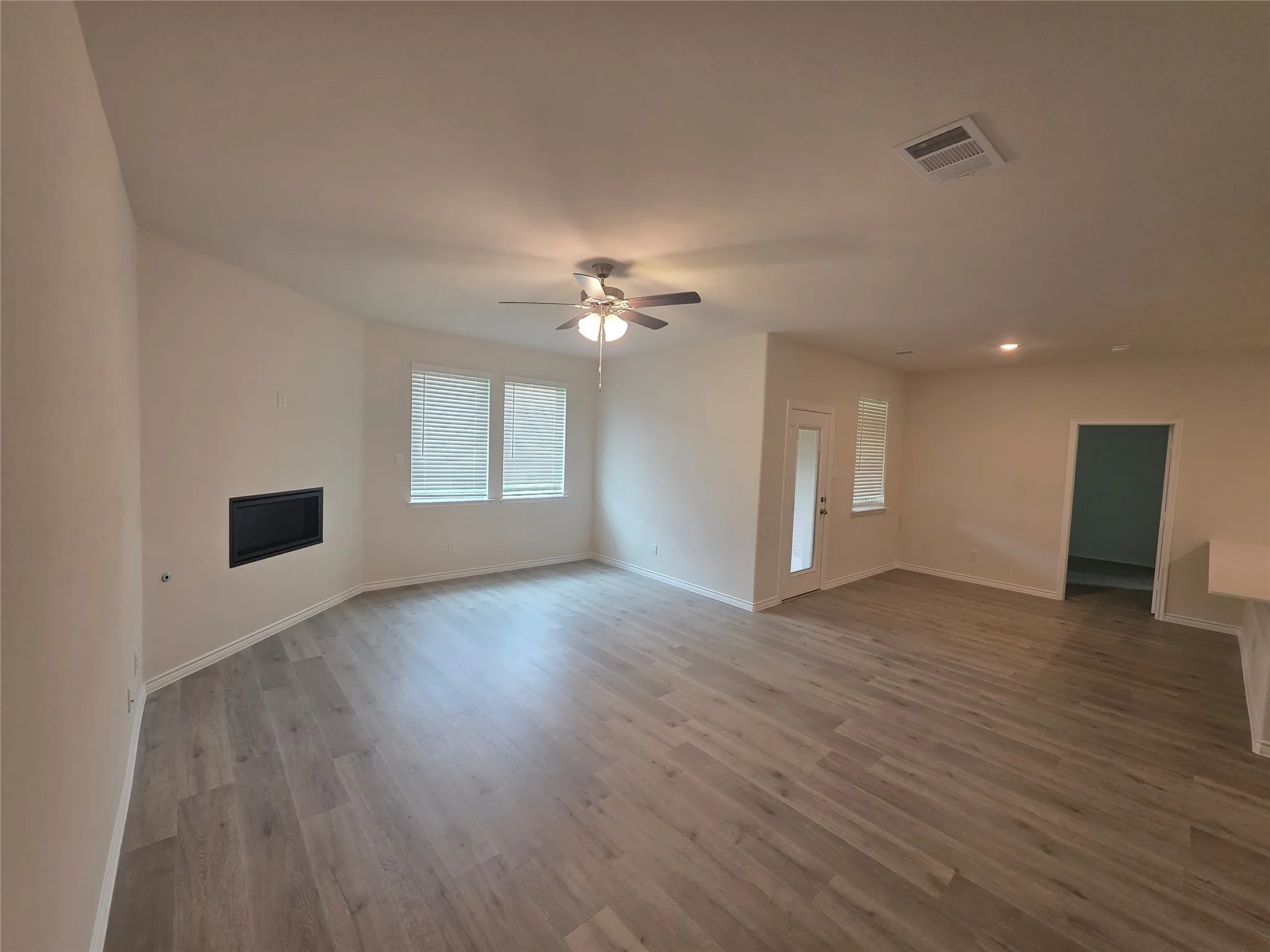 Spacious room with wood-finish flooring, a built-in fireplace, multiple windows with blinds, a ceiling fan with integrated lighting, and recessed ceiling lights