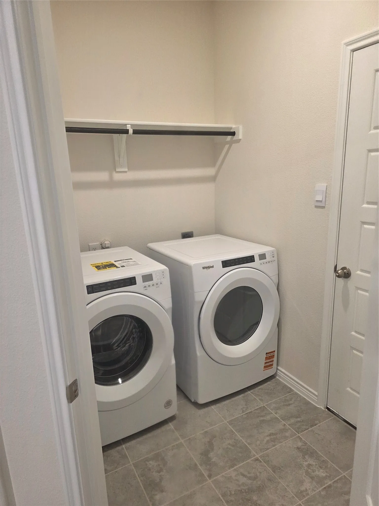 Laundry area featuring a built-in shelf with hanging rod, durable tile flooring, and neutral wall tones