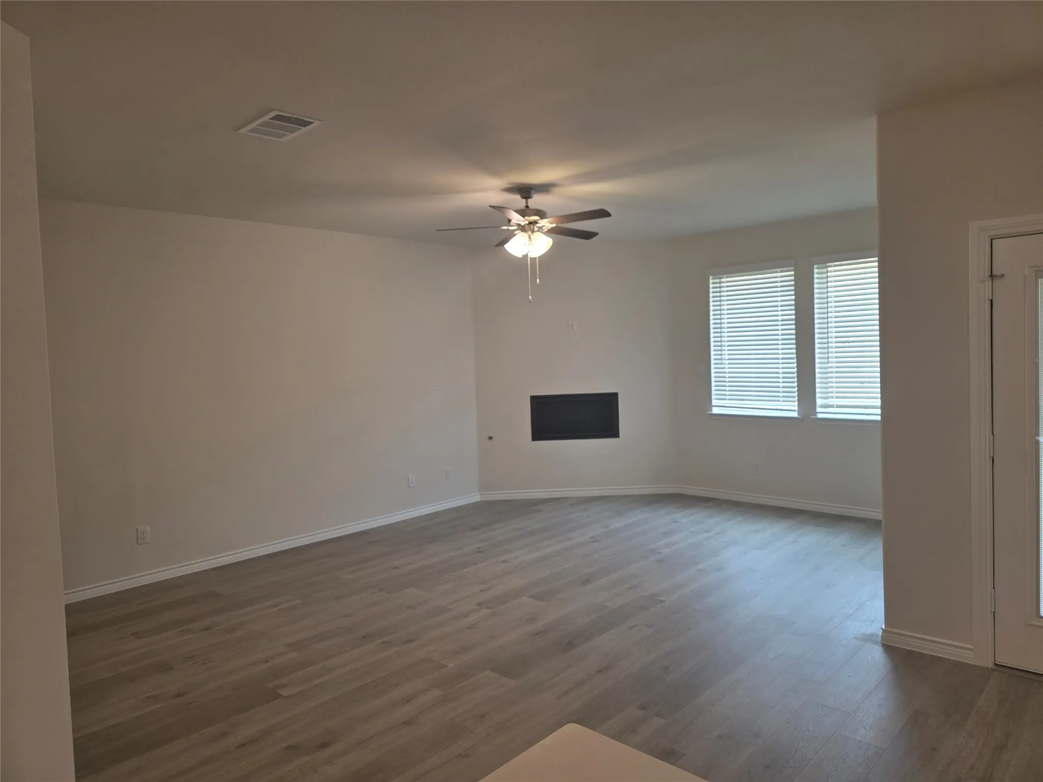 Spacious living area featuring wood-finish flooring, a ceiling fan with integrated lighting, and a wall-mounted insert
