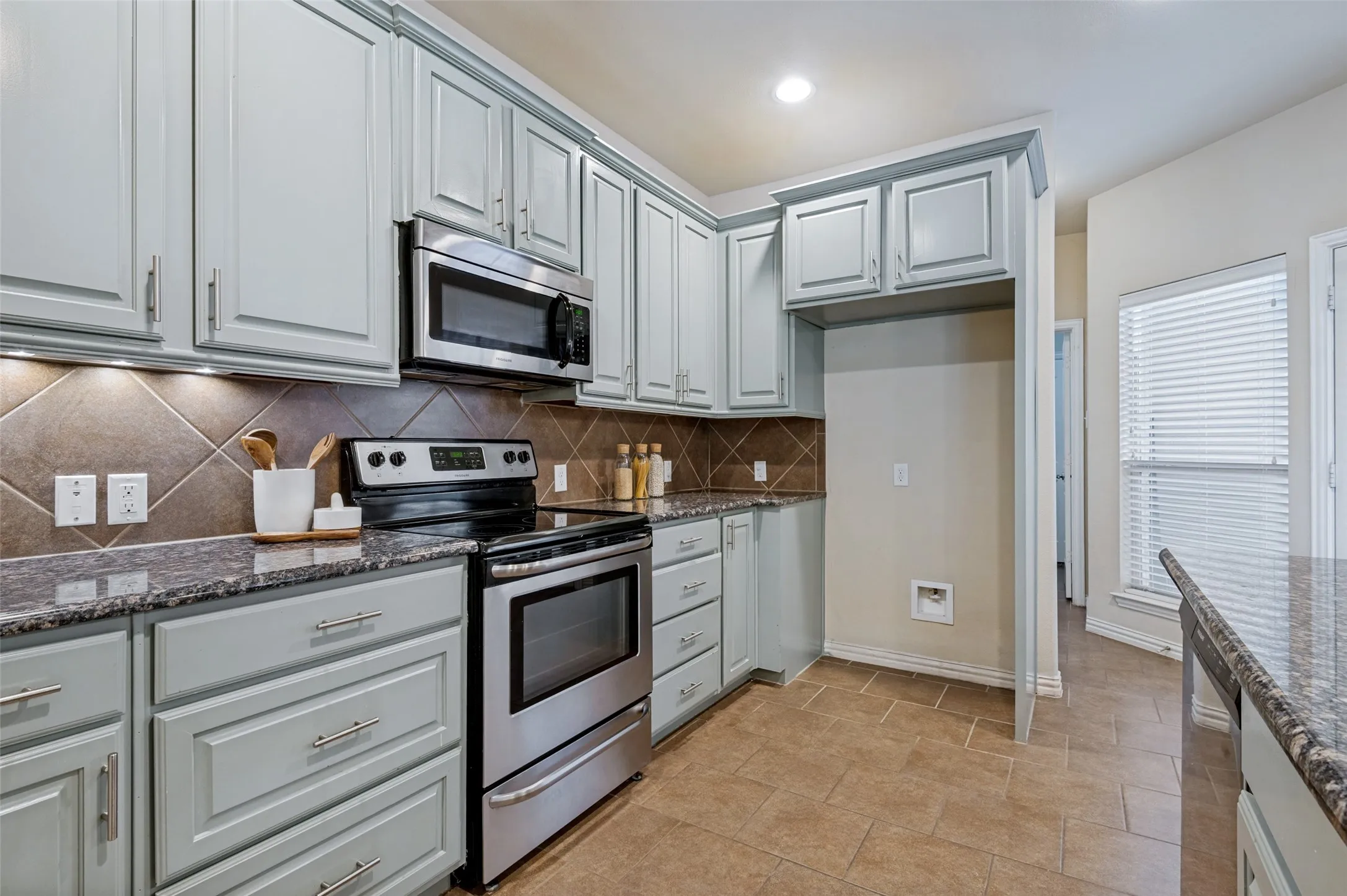 Kitchen featuring light-toned cabinetry, stainless steel appliances, granite countertops, and a tiled backsplash