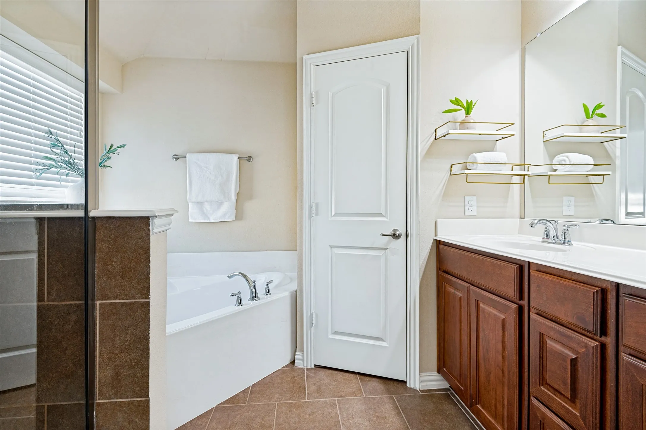 Bathroom with a white soaking tub, separate shower enclosure with ceramic tile surround, and a double vanity featuring wood cabinetry, a light-toned countertop, and a large mirror