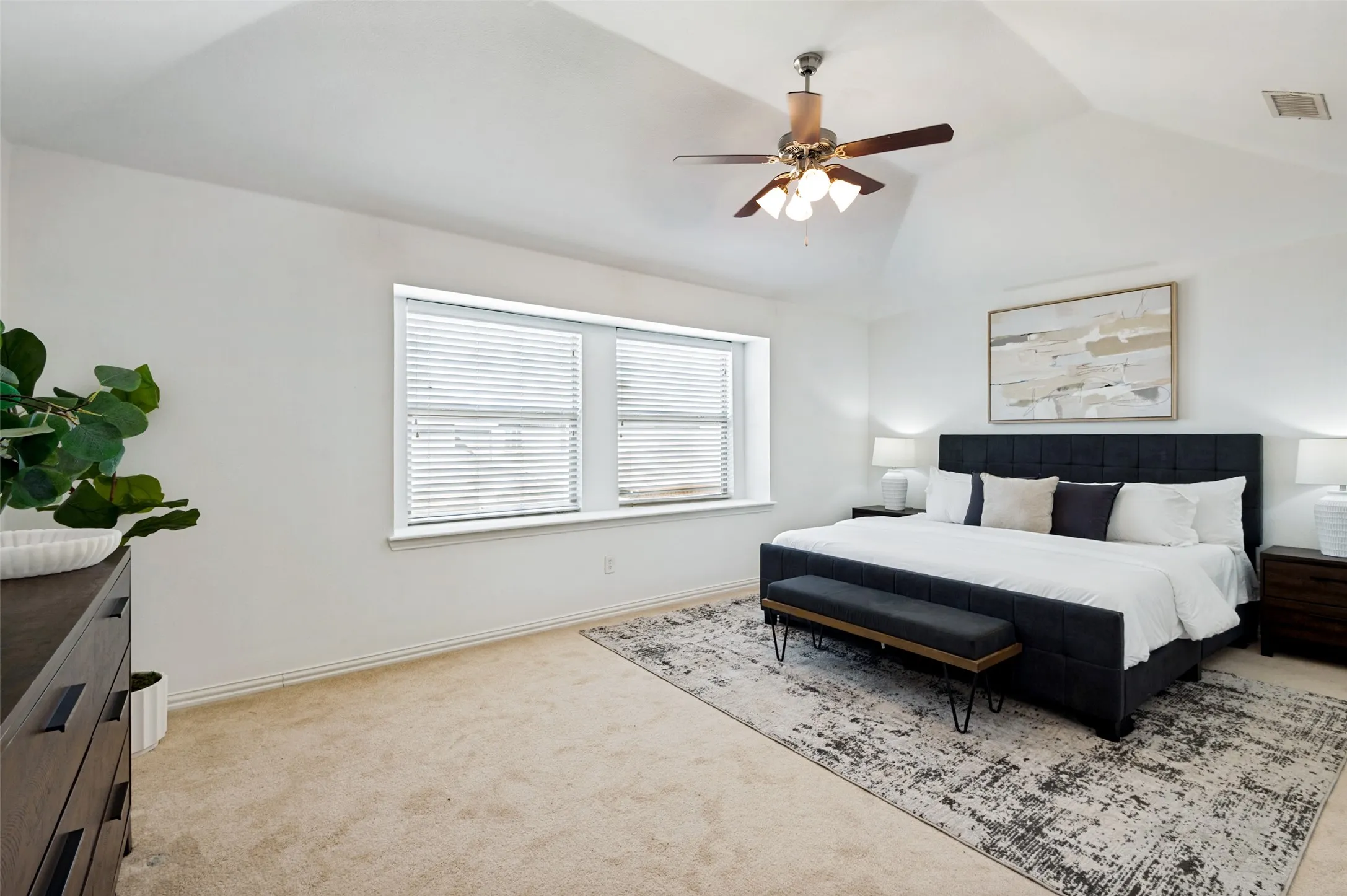 Extra large primary bedroom with ample space for sitting area features vaulted ceiling, carpet flooring, and two large windows with a window bench.