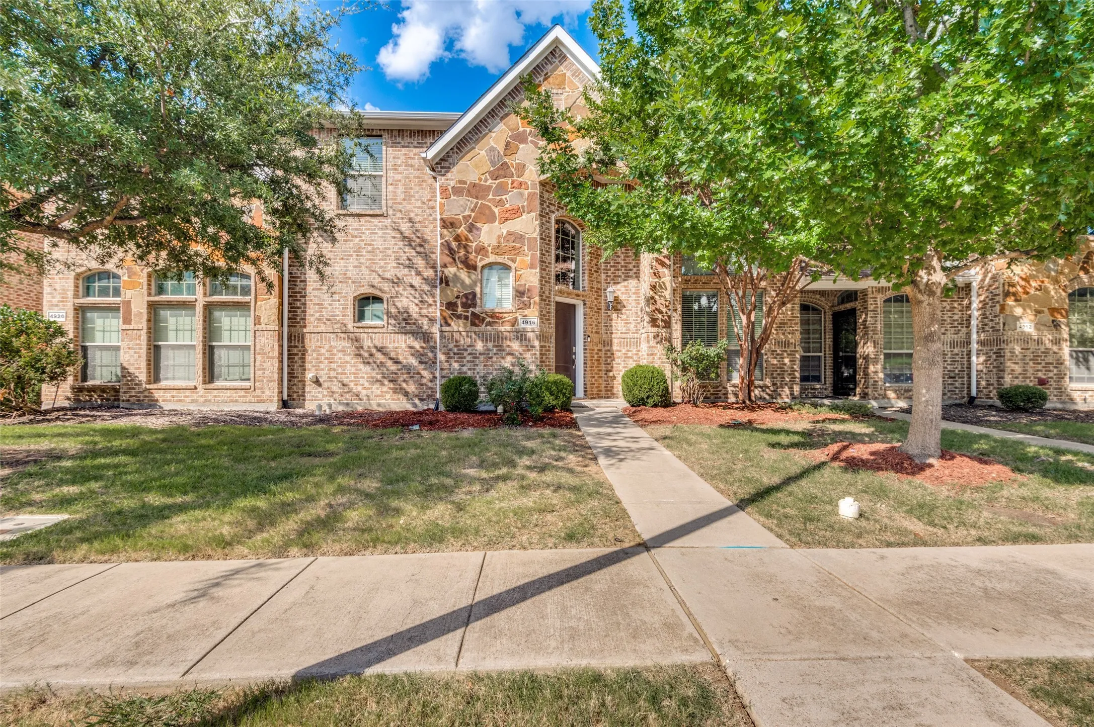 Two-story residential exterior featuring a combination brick and stone facade, multiple arched windows, and a concrete pathway leading to the entry