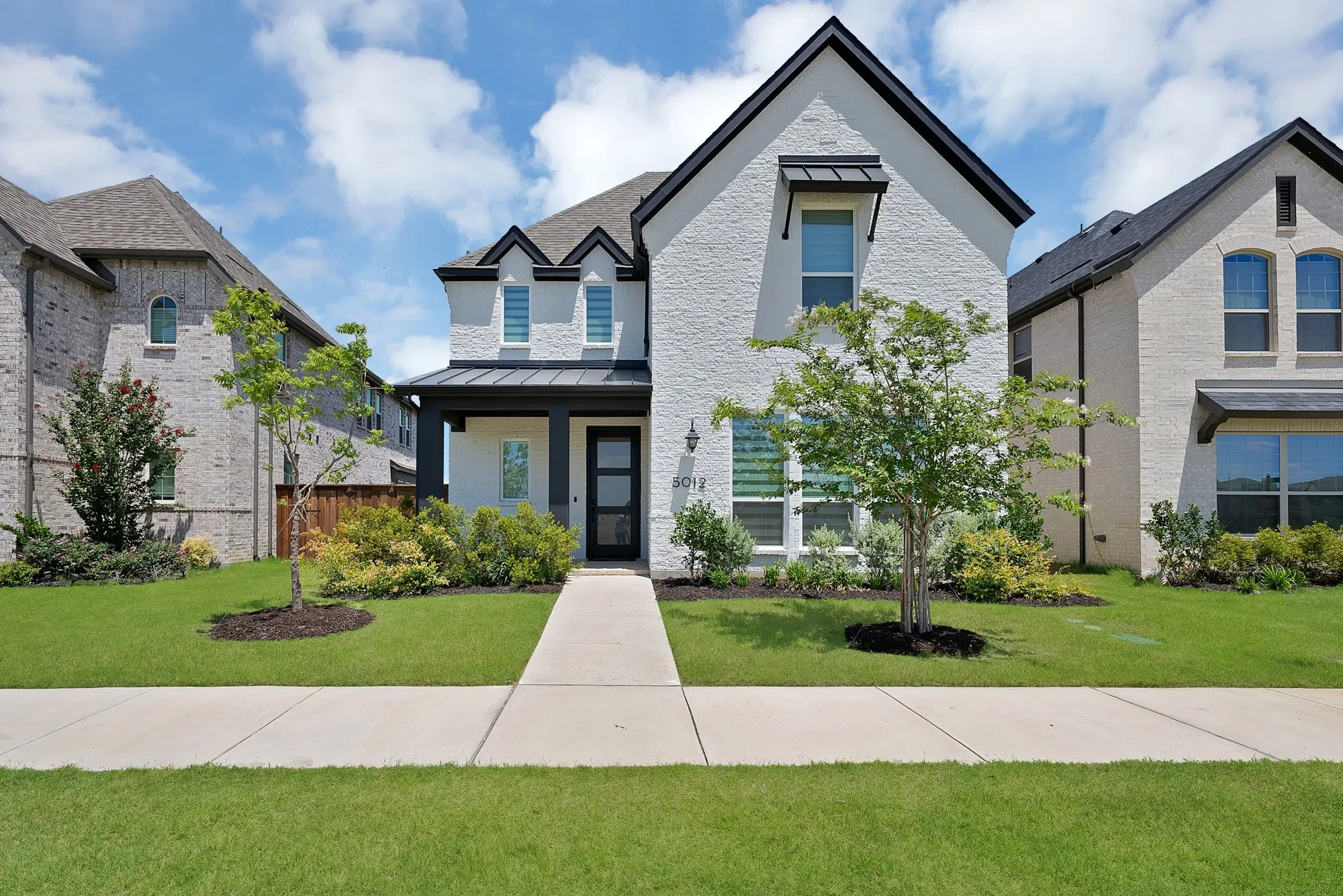 White brick facade featuring black trim accents, a prominent front gable, and a covered entry