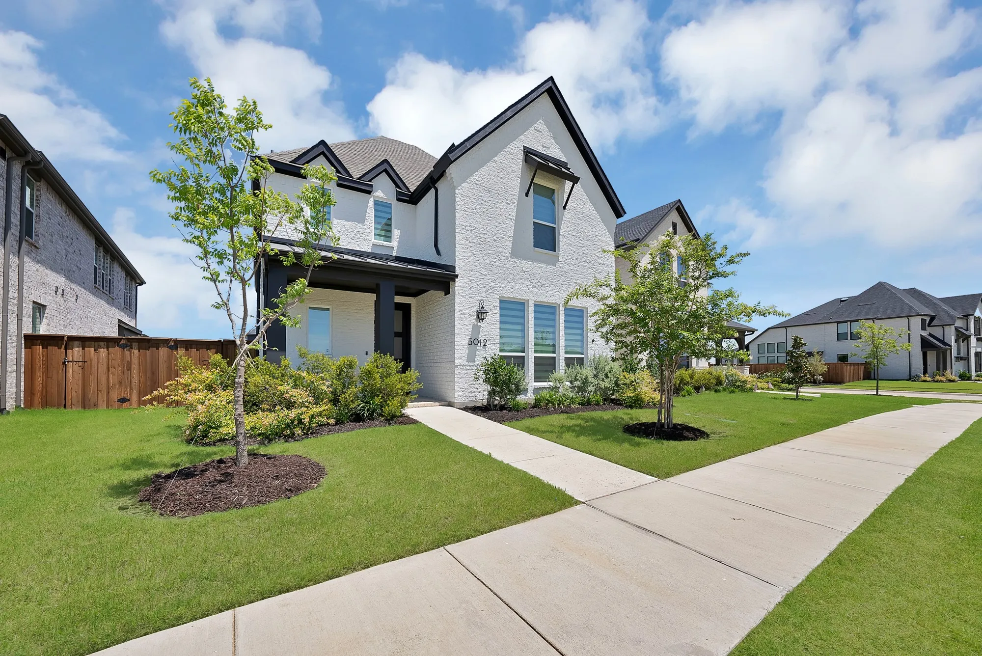 White brick exterior with contrasting dark trim, featuring a covered entry and decorative window awnings