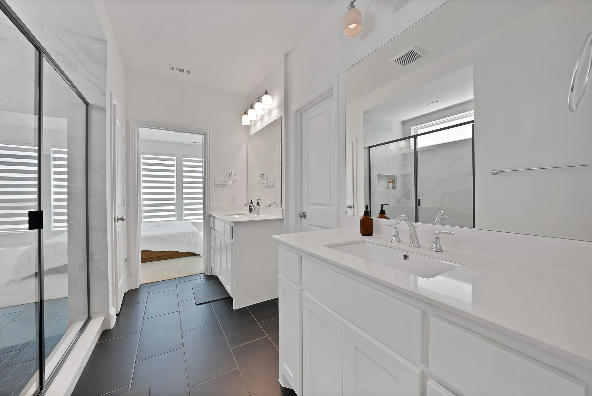Dual vanity bathroom featuring stone countertops, integrated sinks, white cabinetry, and matte black tile flooring