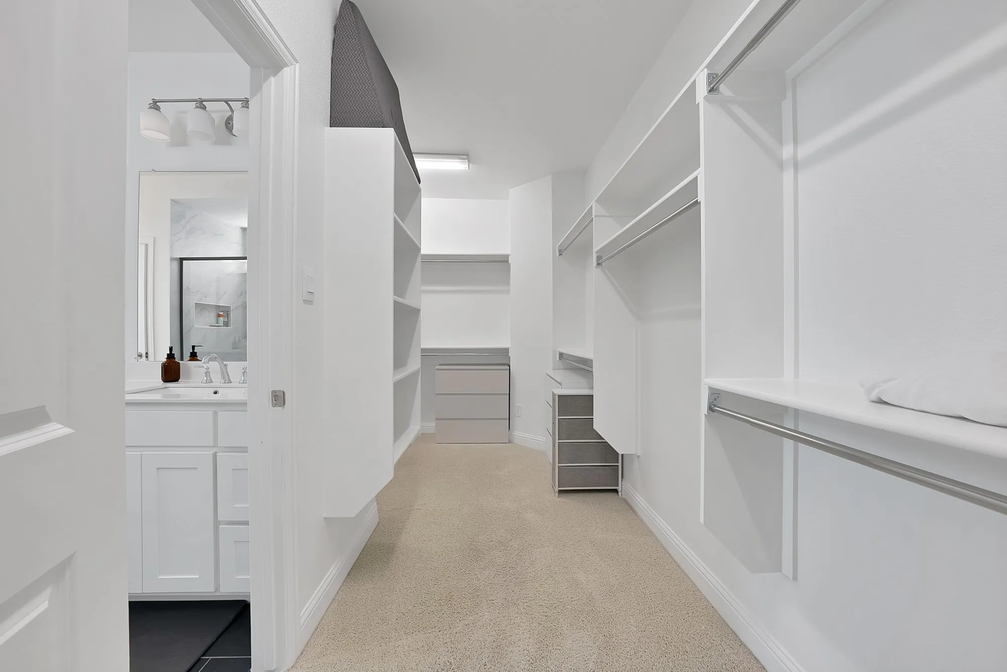 Walk-in closet with extensive built-in shelving, hanging rods, central storage island with drawers, and neutral carpeting