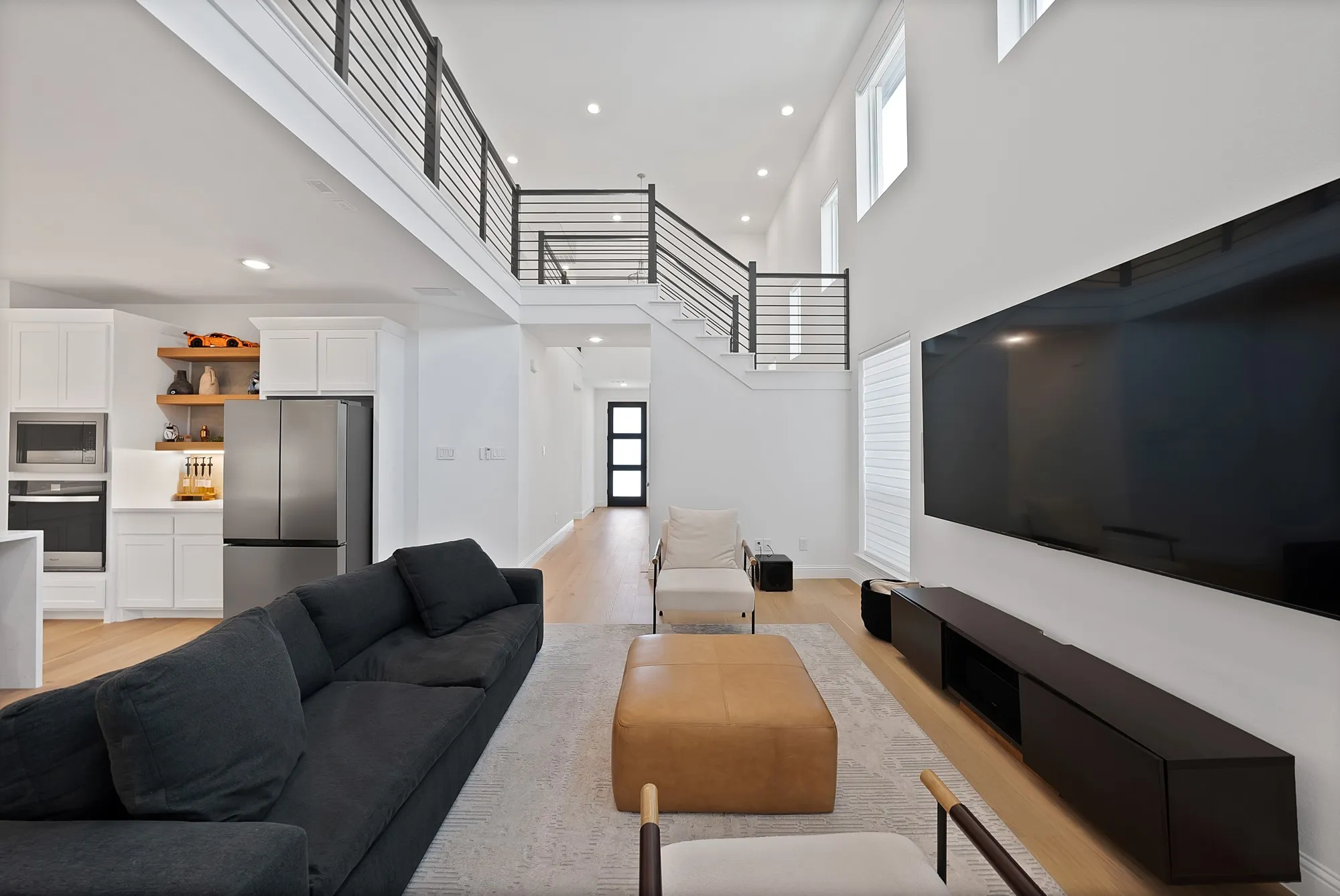 Open-concept living area with a double-height ceiling, light wood-finish flooring, and a modern stair railing