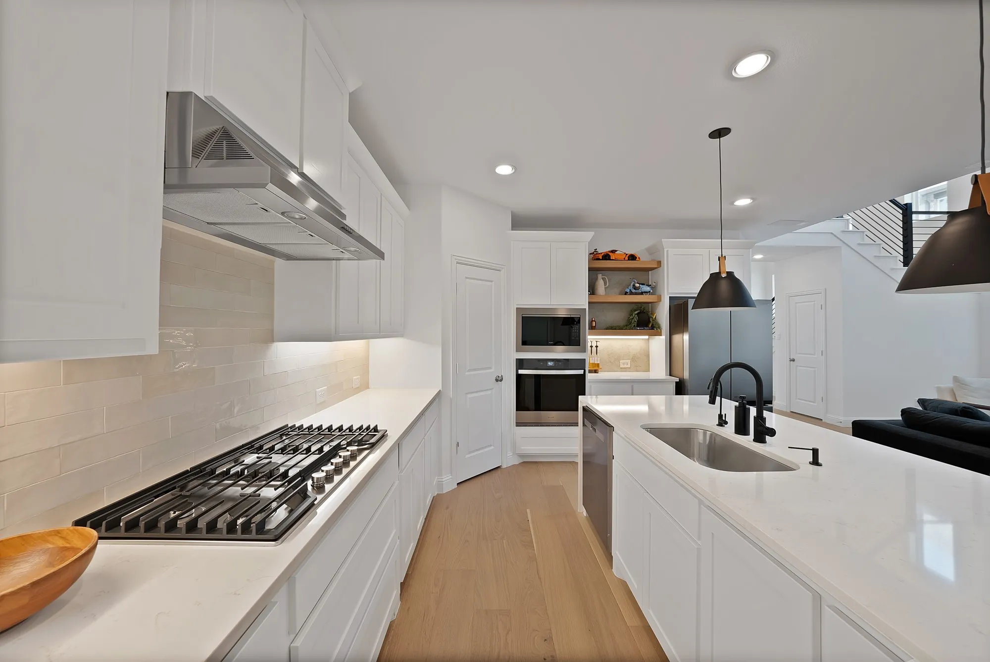 Modern kitchen featuring light wood-finish flooring, white cabinetry, integrated stainless steel appliances, and an expansive island with an undermount sink and matte black fixtures