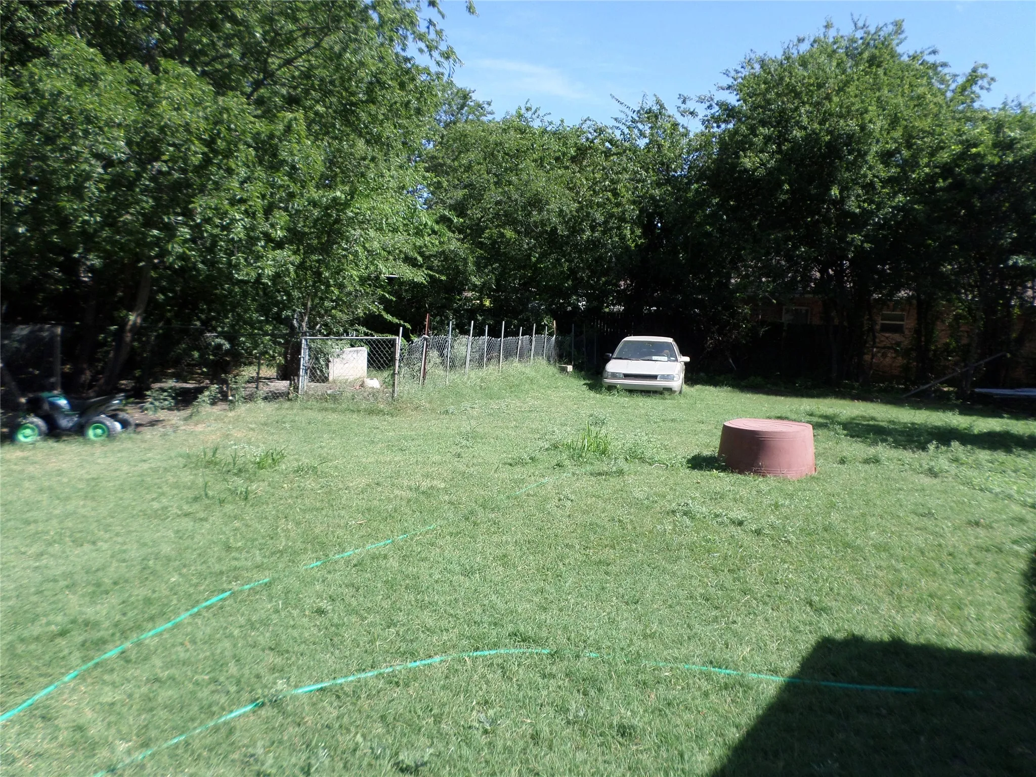 Expansive grassy area with mature perimeter trees and a chain-link fence