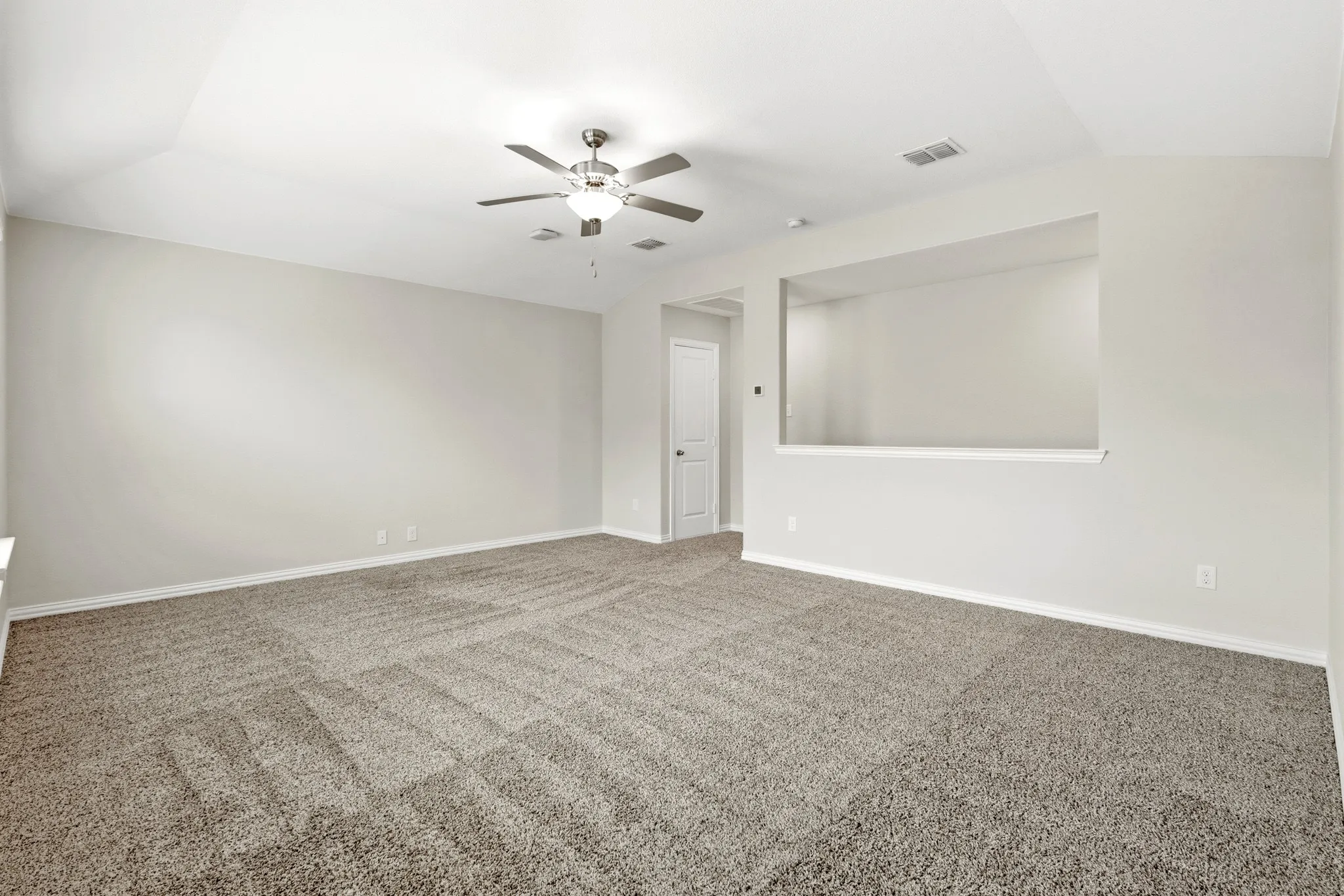 Spacious room featuring vaulted ceilings, a ceiling fan with integrated lighting, soft neutral-toned carpet, and a decorative wall cutout