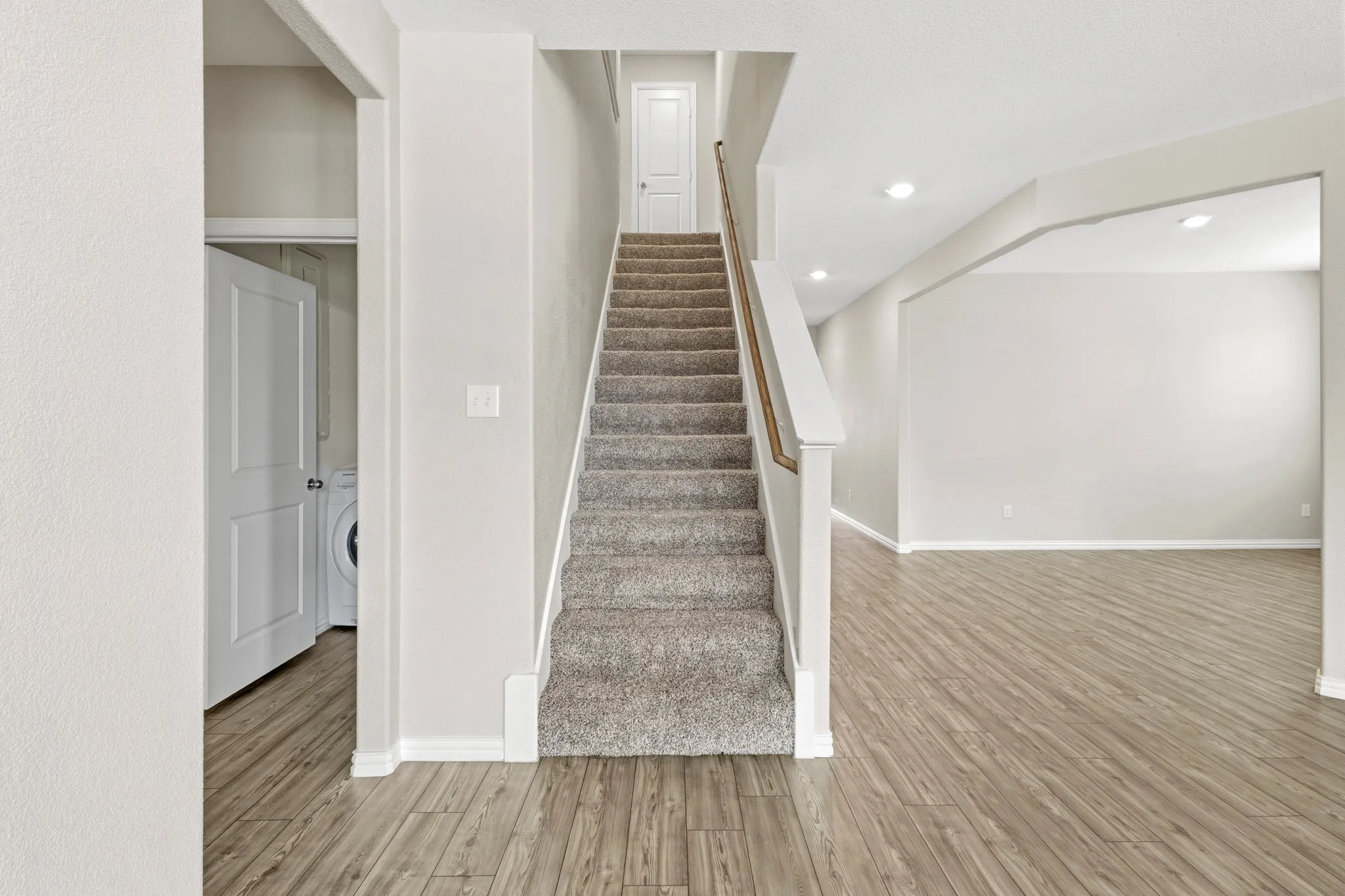 Carpeted staircase with white balusters and wood-finish handrail