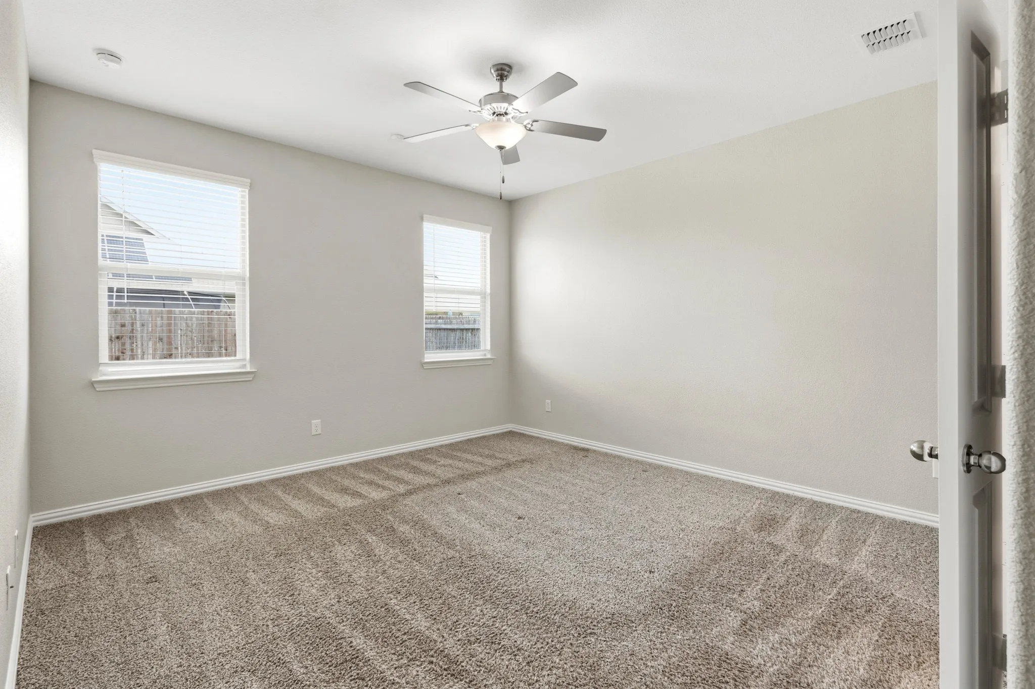 Carpeted room featuring two double-hung windows with blinds, a ceiling fan with integrated lighting, and neutral wall paint