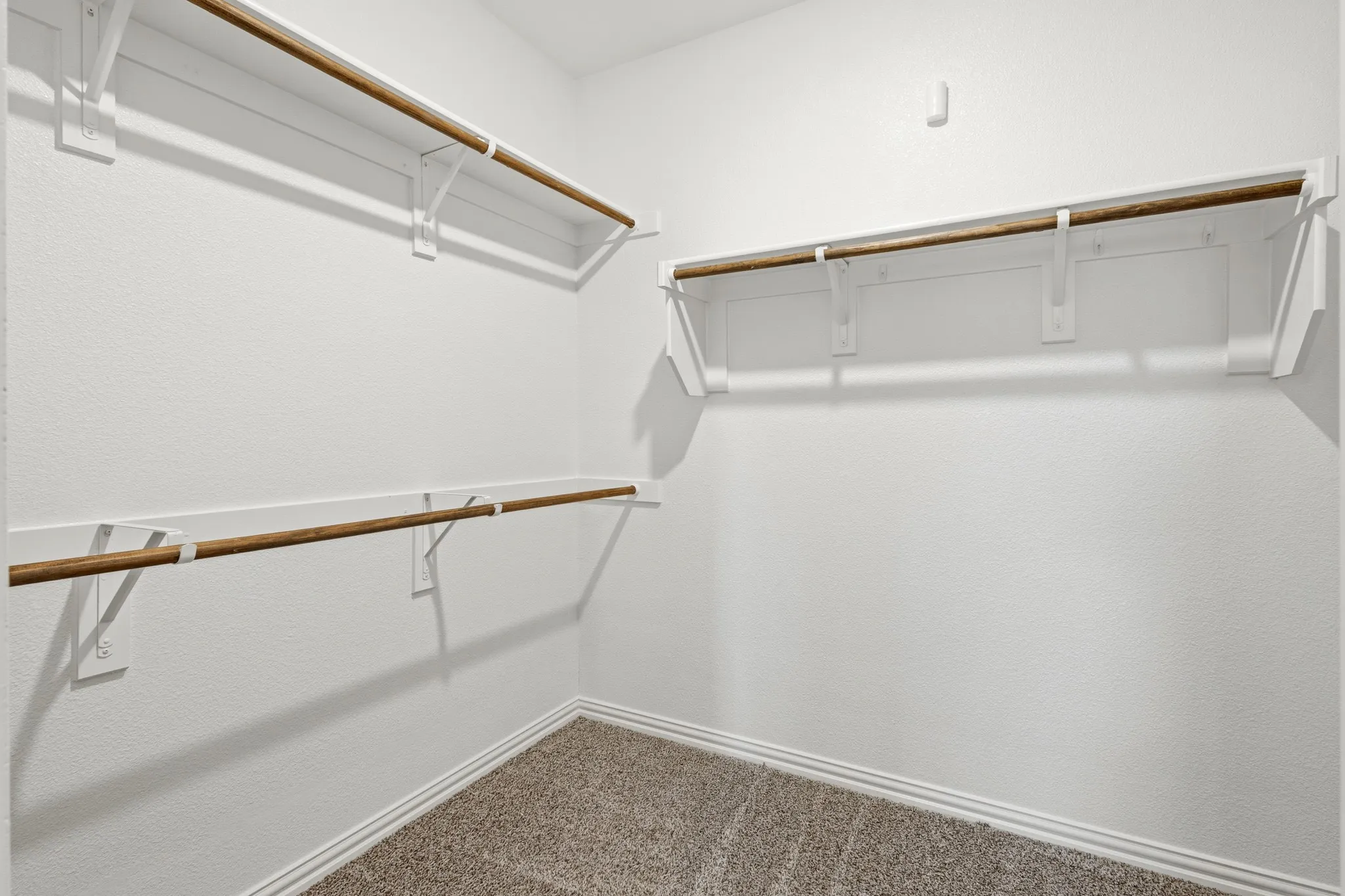 Walk-in closet featuring white painted shelving and wood-finish hanging rods