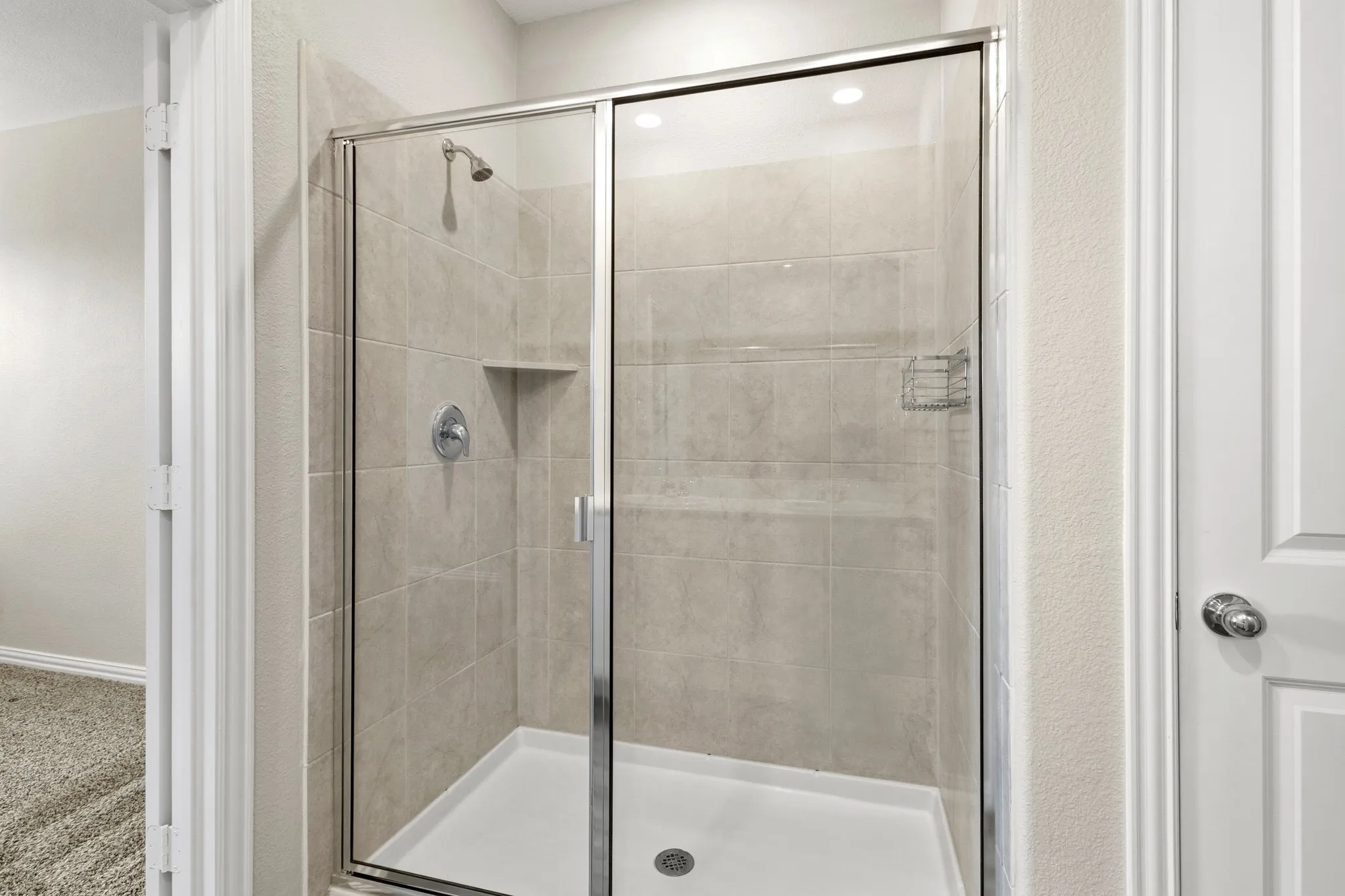 Walk-in shower featuring a chrome-framed glass enclosure, light-toned tile surround, built-in shower niche, and a white shower pan