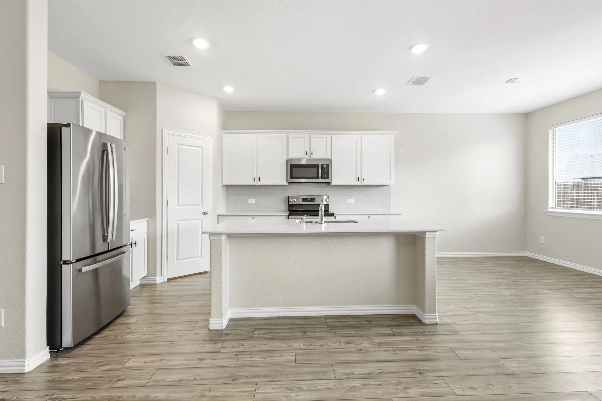 Open-concept kitchen featuring an island with a sink, white cabinetry, stainless steel appliances, and wood-finish flooring