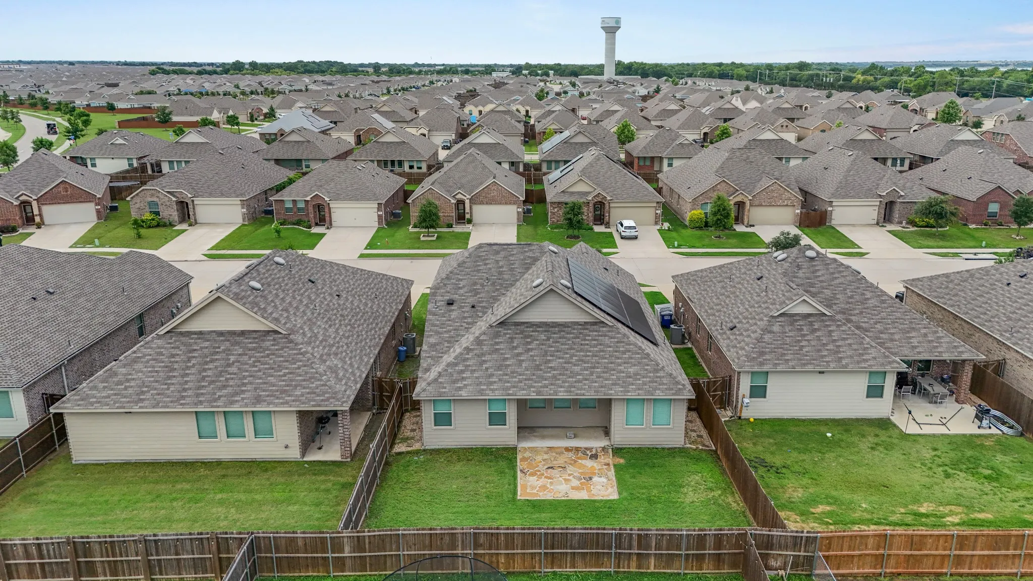Rear exterior featuring a stone patio, fenced backyard, and multiple roof-mounted solar panels