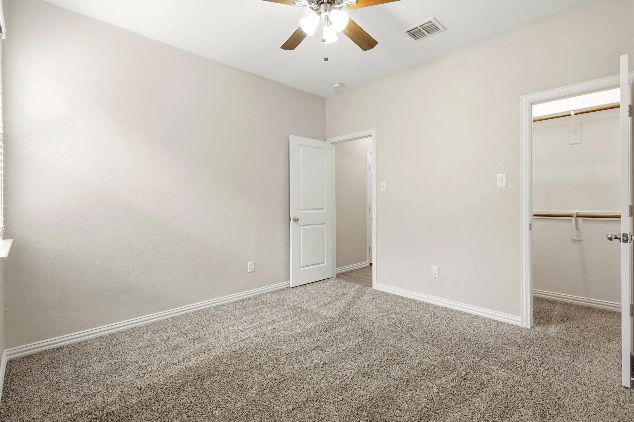 Carpeted room featuring a ceiling fan with light fixture, neutral wall paint, and white baseboards