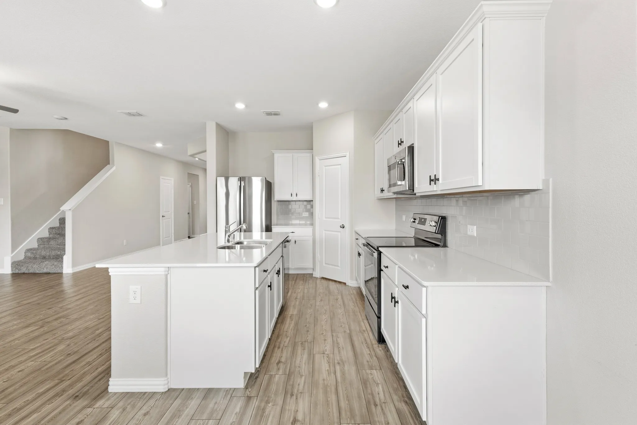 Modern kitchen featuring a large central island with double sink, white cabinetry, integrated stainless steel appliances, white countertops, and a tiled backsplash