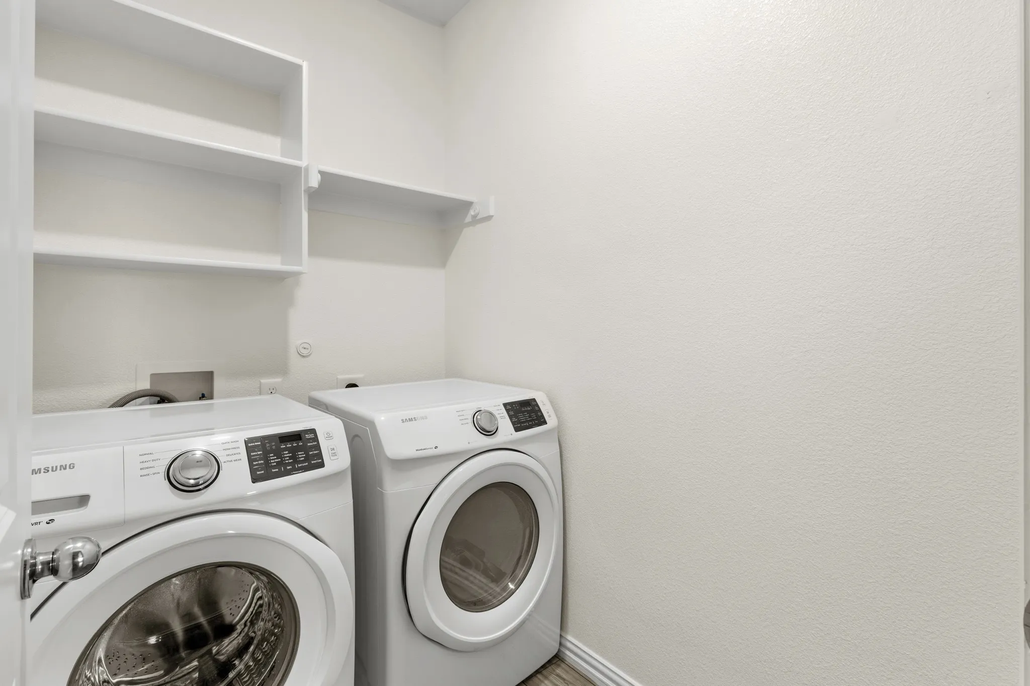 Dedicated laundry area featuring white walls, ample built-in shelving, and wood-finish flooring