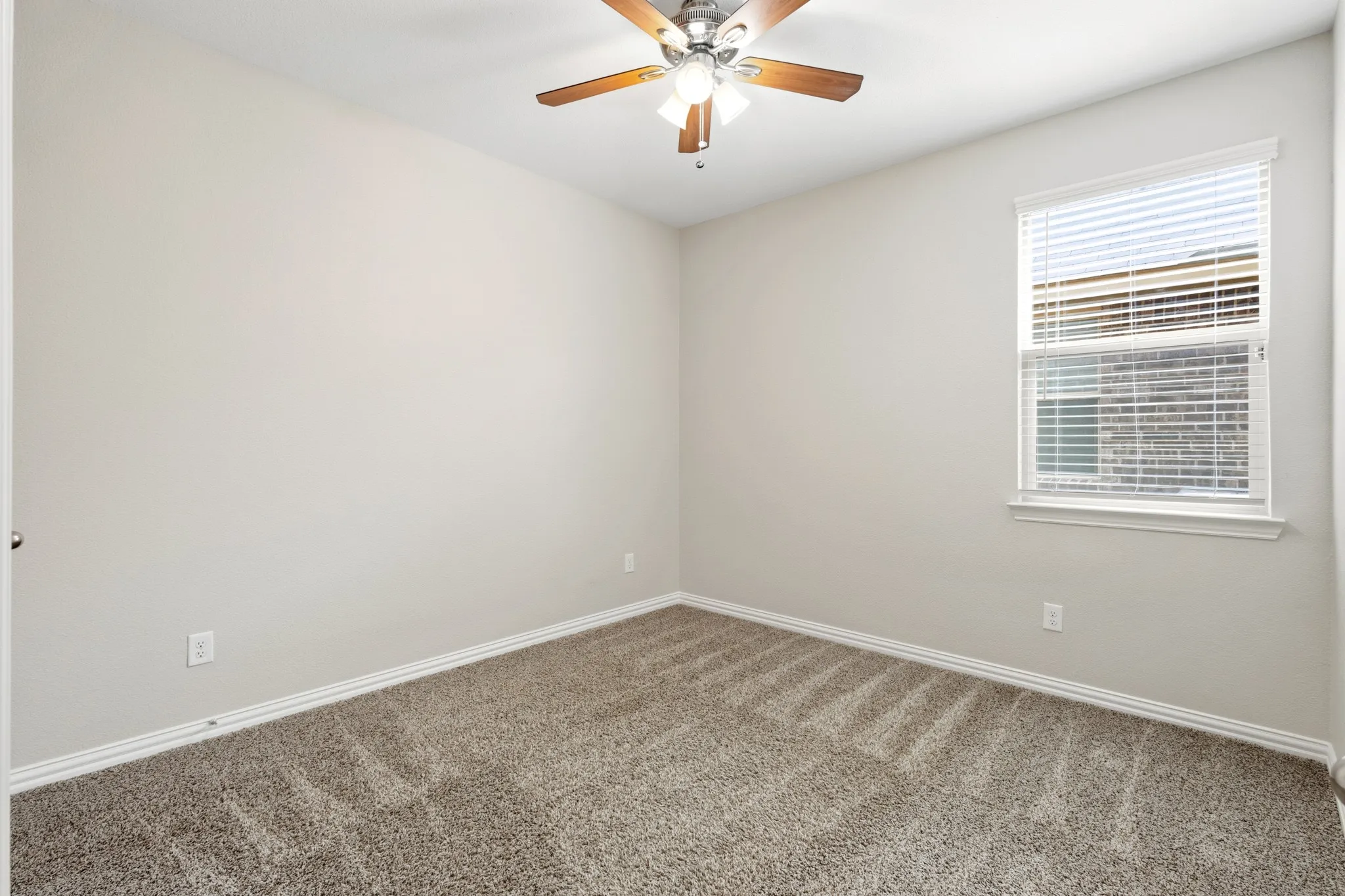 Carpeted interior room featuring a window with blinds, a ceiling fan with integrated lighting, light-toned walls, and white baseboards