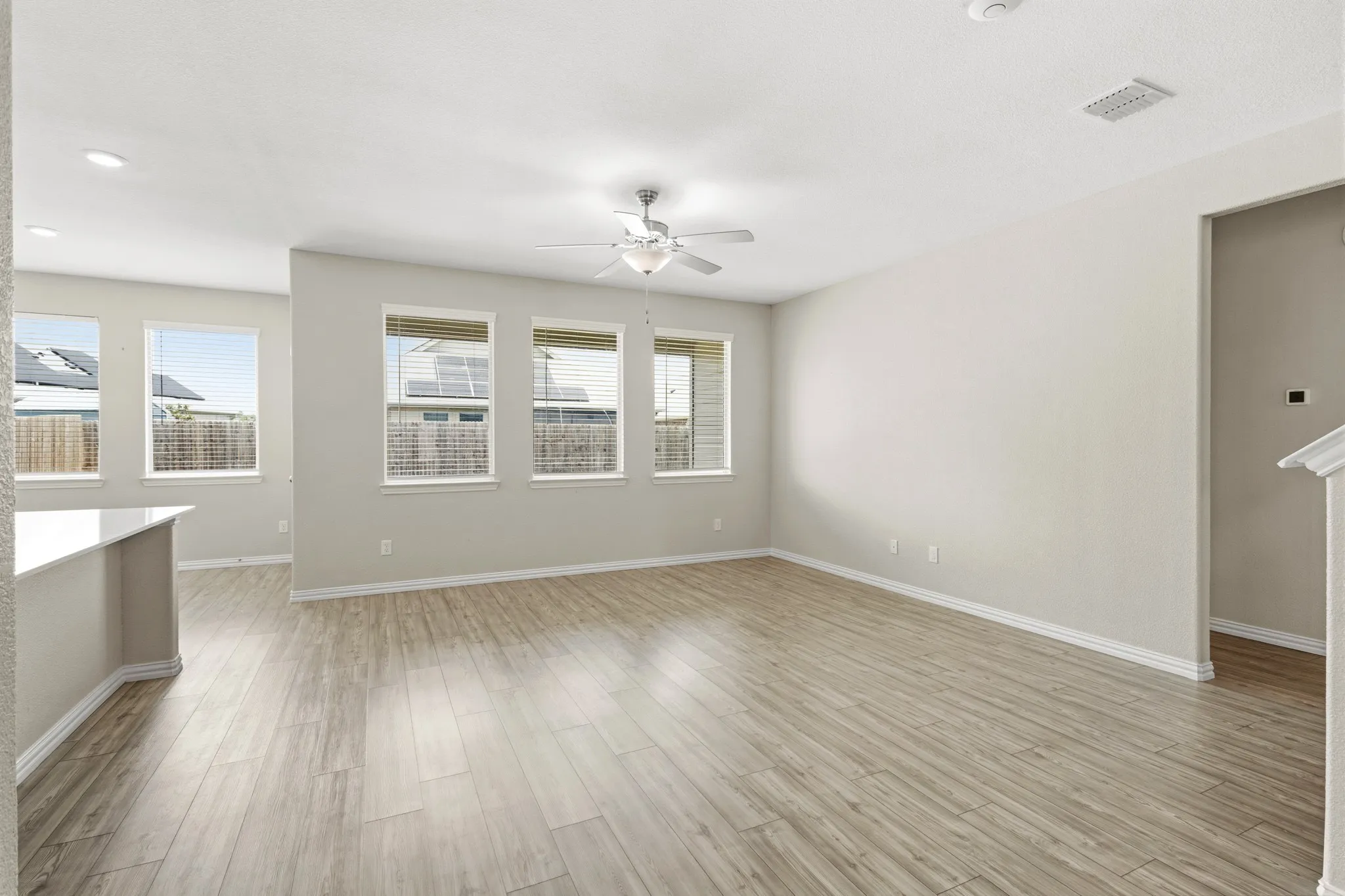 Spacious living area featuring light wood-finish flooring, recessed lighting, and multiple windows with blinds