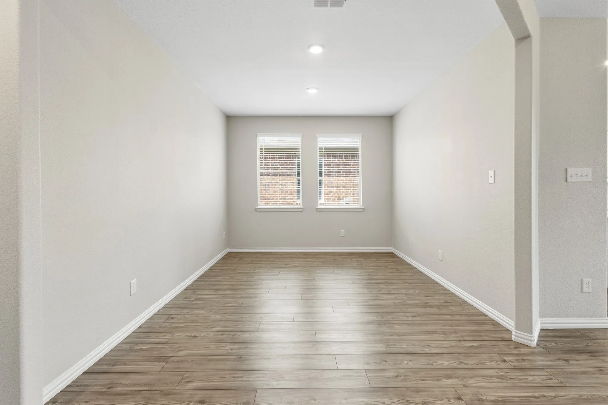 Spacious interior room featuring wood-finish flooring, two windows with blinds, recessed lighting, and light-toned walls