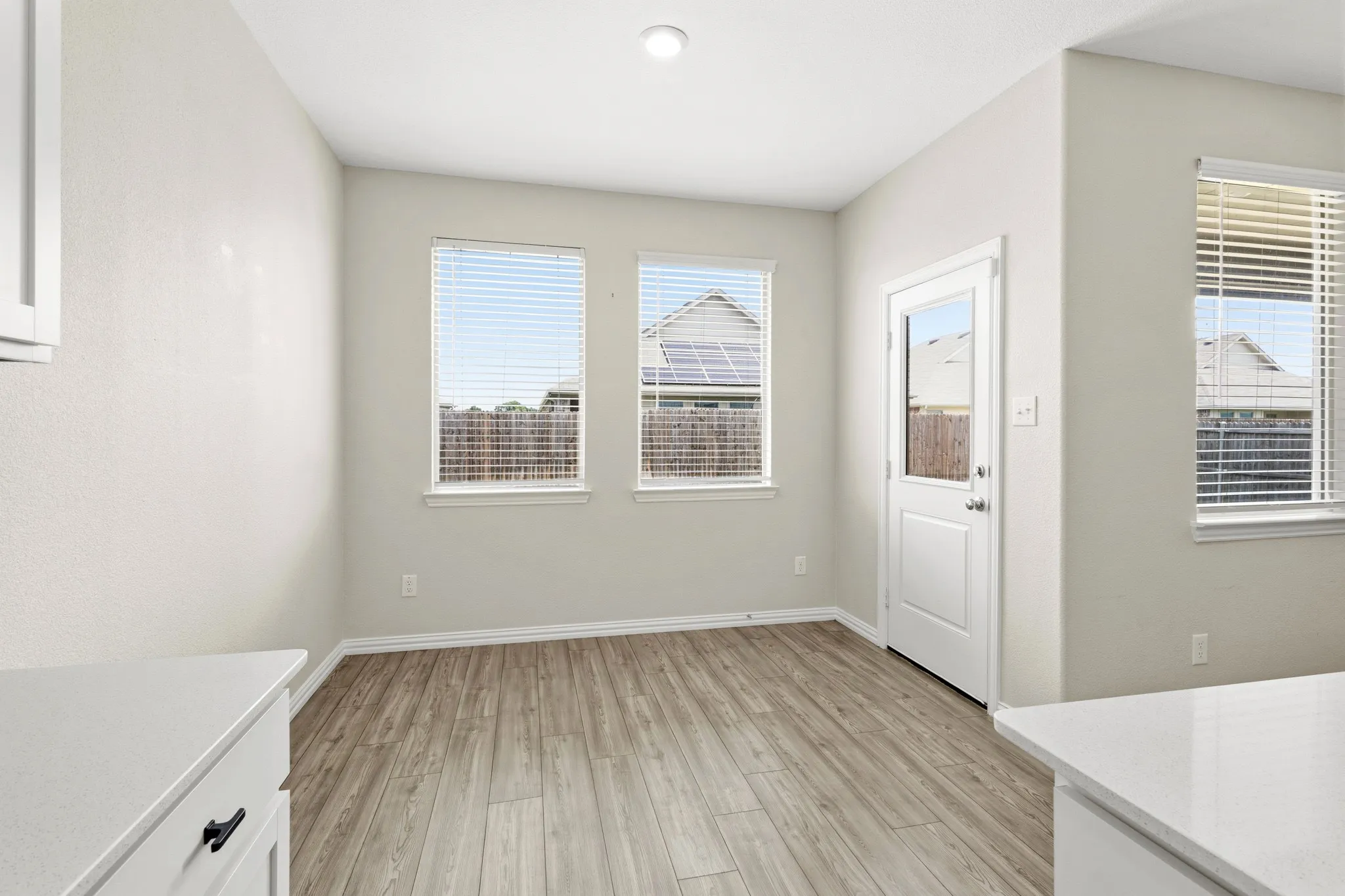 Open-concept room featuring wood-finish flooring, two large windows, a white glass-panel door, and recessed lighting
