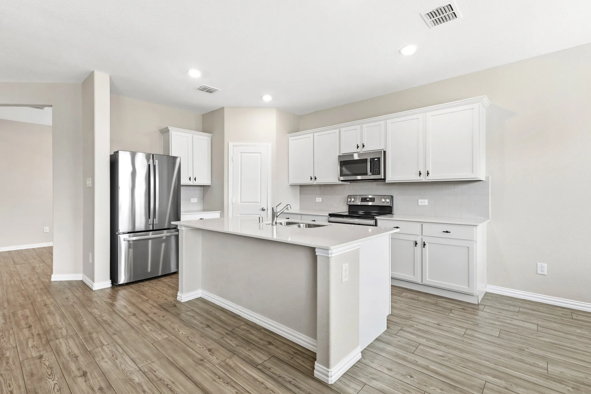 Kitchen featuring white shaker cabinetry, stainless steel appliances, a center island with sink, light-toned countertops, and wood-finish flooring