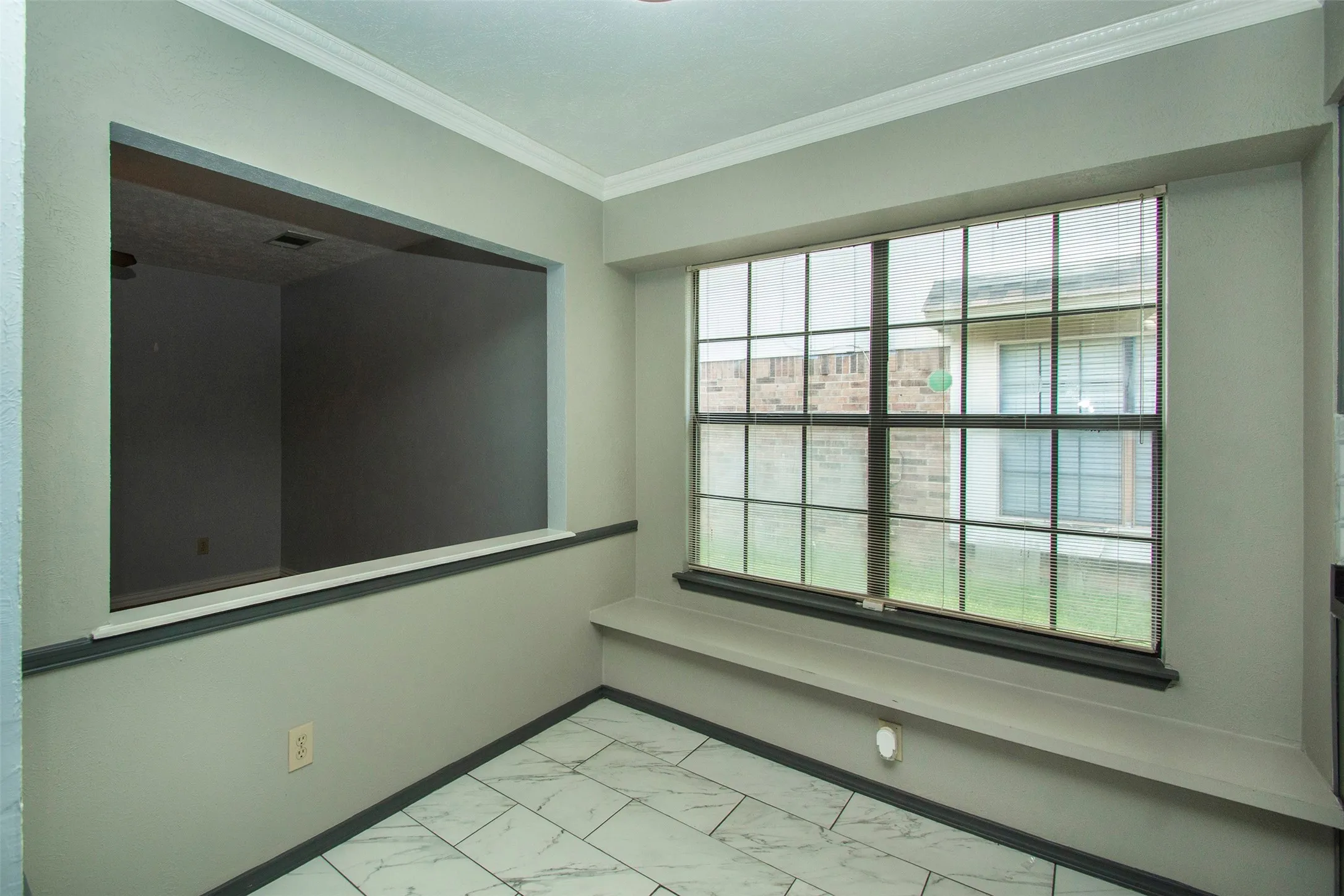 Windowed eating area featuring a large grid-pattern window, built-in window bench, and white marble-look tile flooring