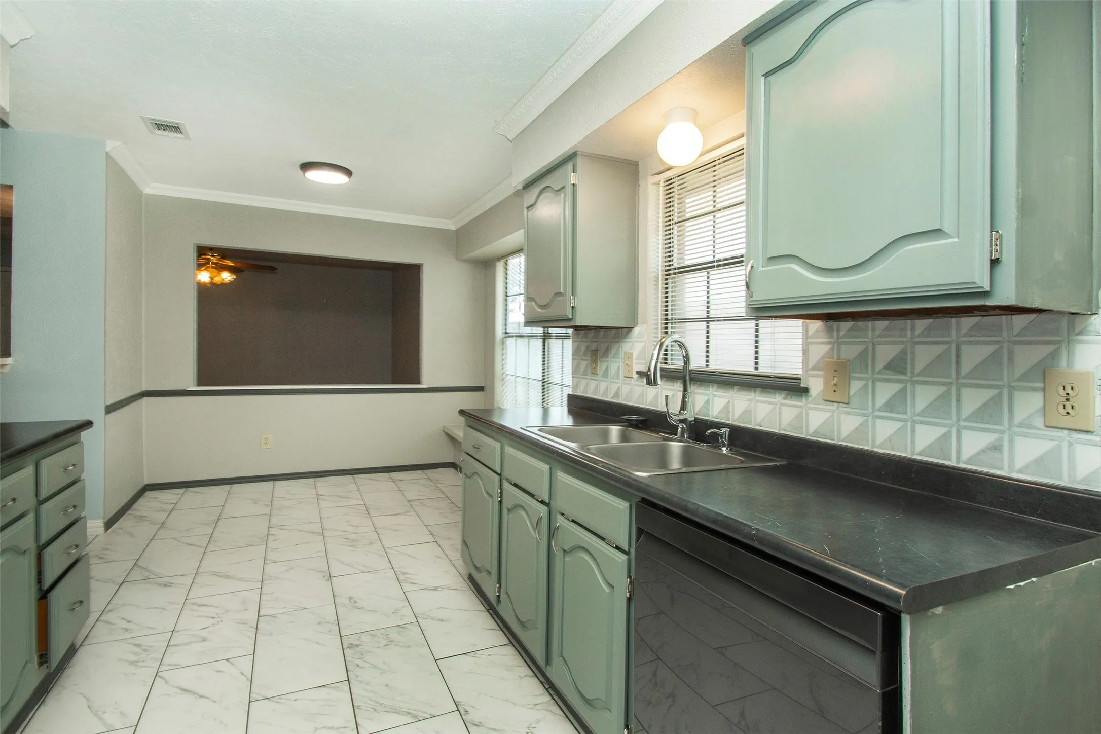 Kitchen featuring light-colored cabinetry, black countertops, a stainless steel double basin sink, and a geometric tile backsplash
