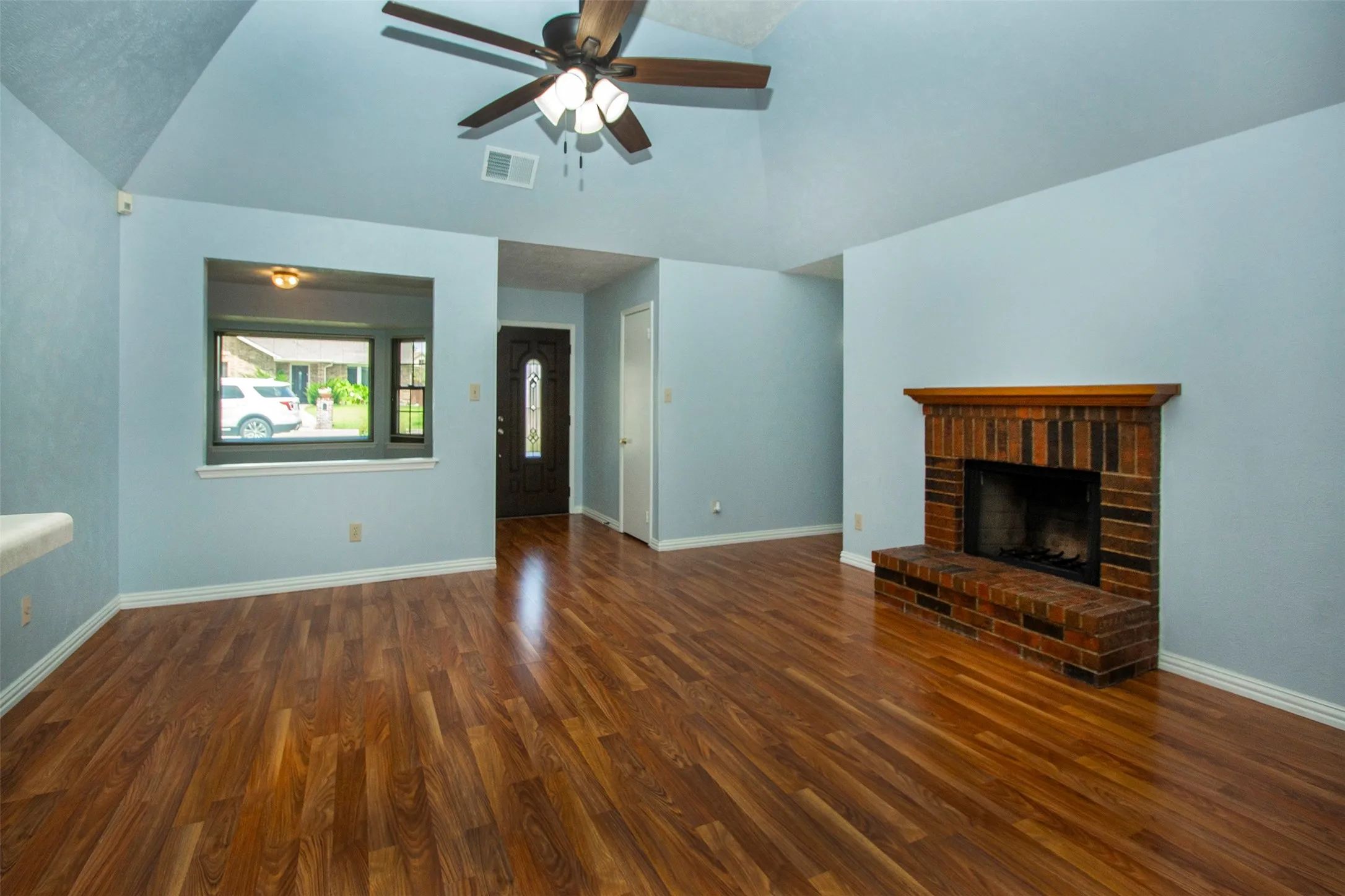 Wood-finish flooring throughout, complemented by a brick fireplace with a wood mantel