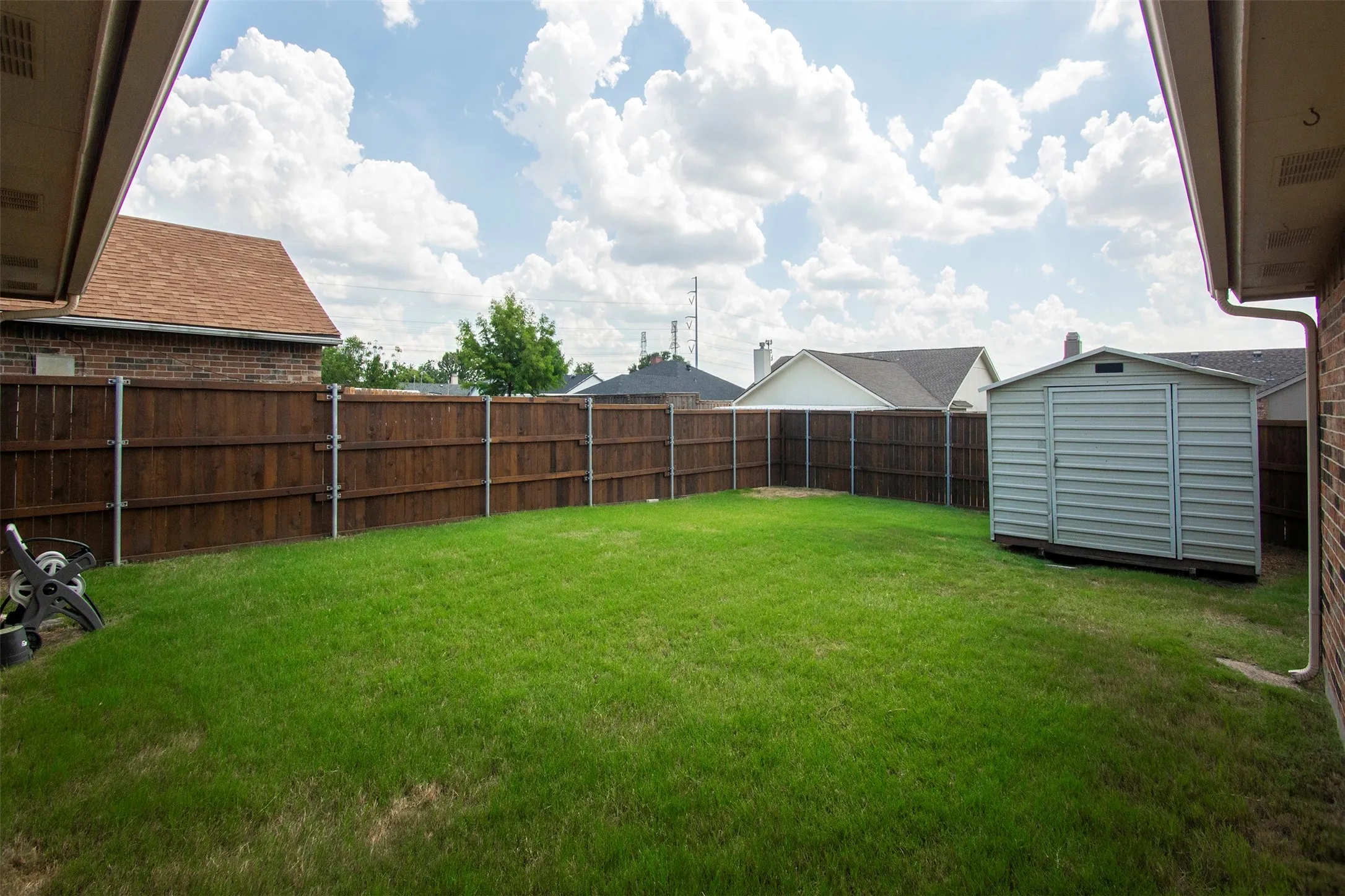 Expansive backyard featuring a lush lawn, privacy fencing, and a detached storage shed