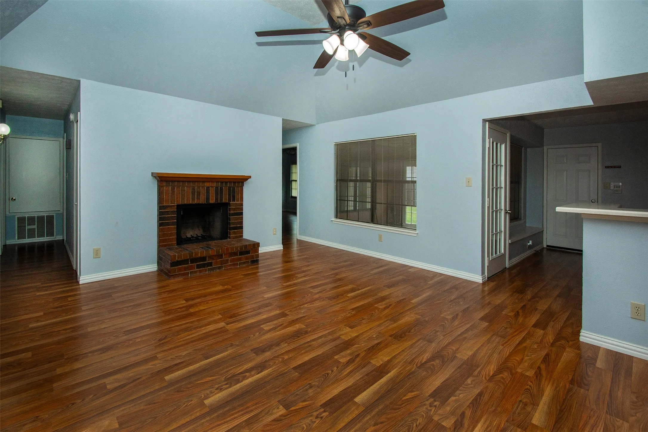 Living area featuring wood-finish flooring, a brick fireplace with a wood mantle, and a vaulted ceiling with a ceiling fan