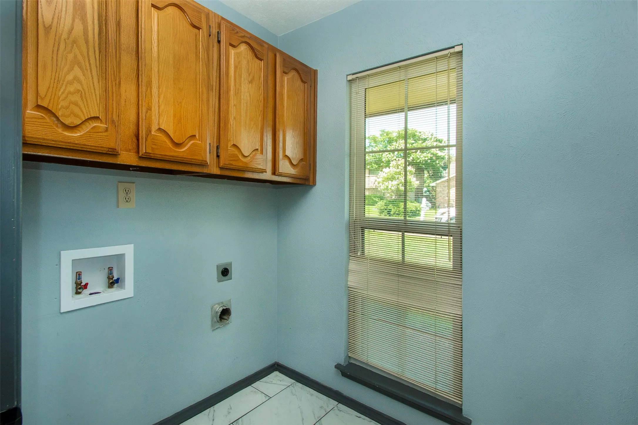 Laundry area featuring wood cabinetry, a window with horizontal blinds, and a tile floor