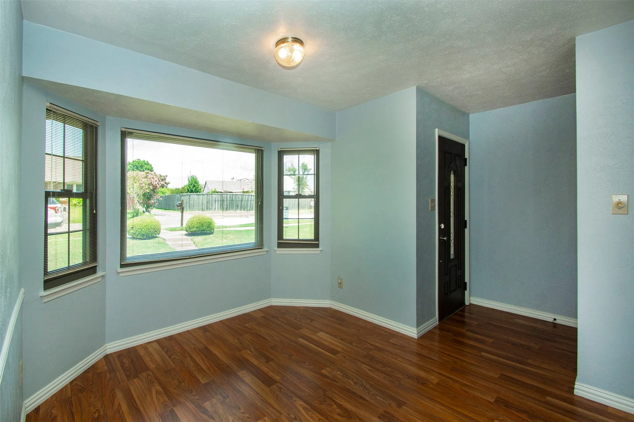 Hardwood-finish flooring throughout, featuring a bay window with multiple panes and a prominent entryway door with decorative glass inserts
