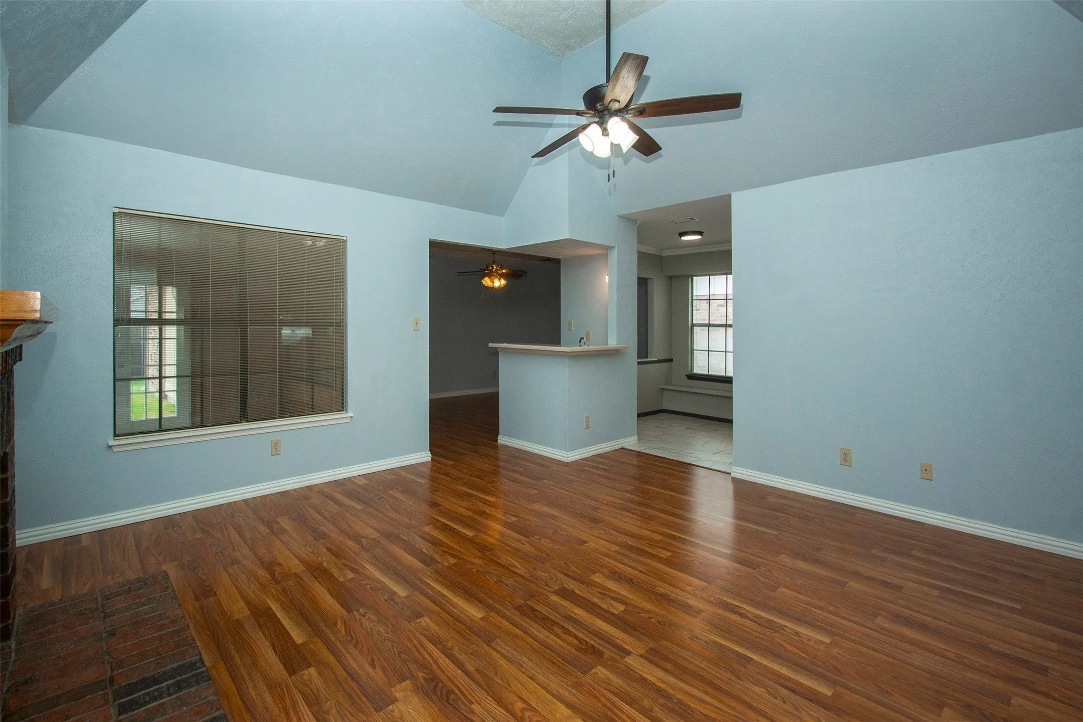 Spacious living area featuring vaulted ceilings, wood-finish flooring, and a brick fireplace