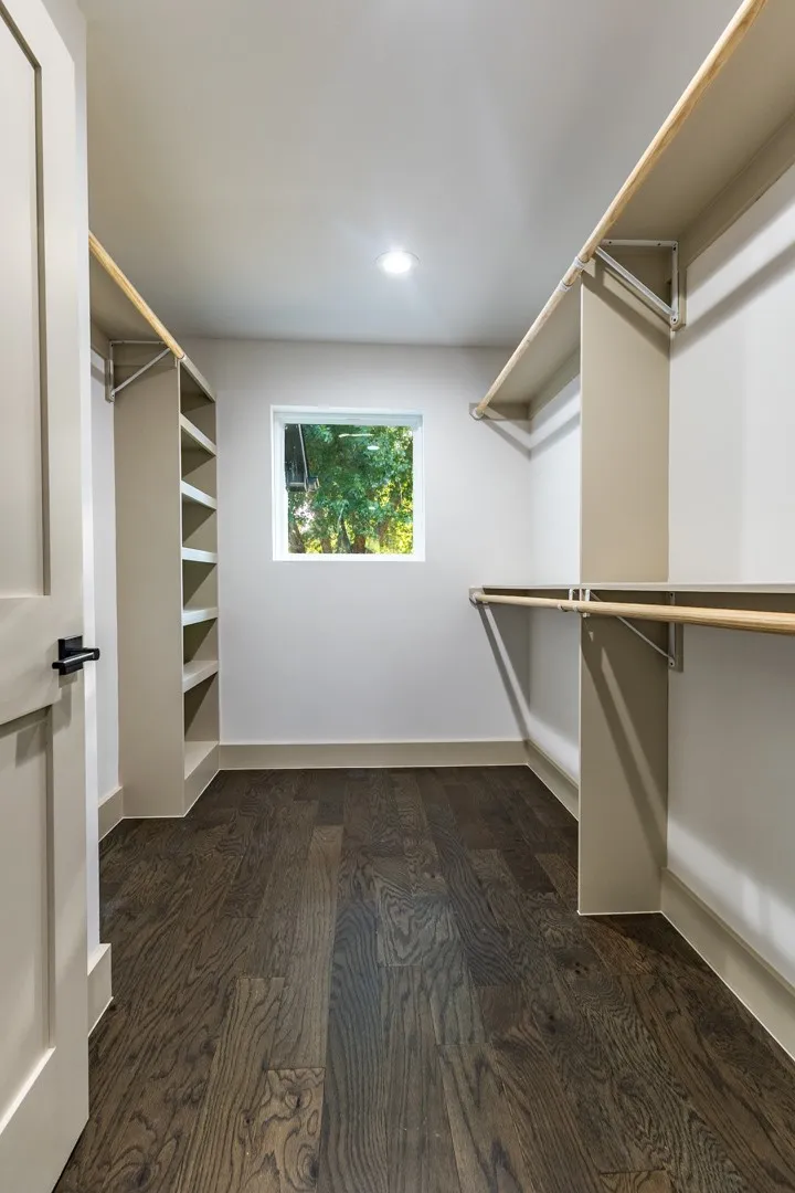 First primary Walk-in closet featuring extensive built-in shelving, hanging rods, and dark wood-finish flooring