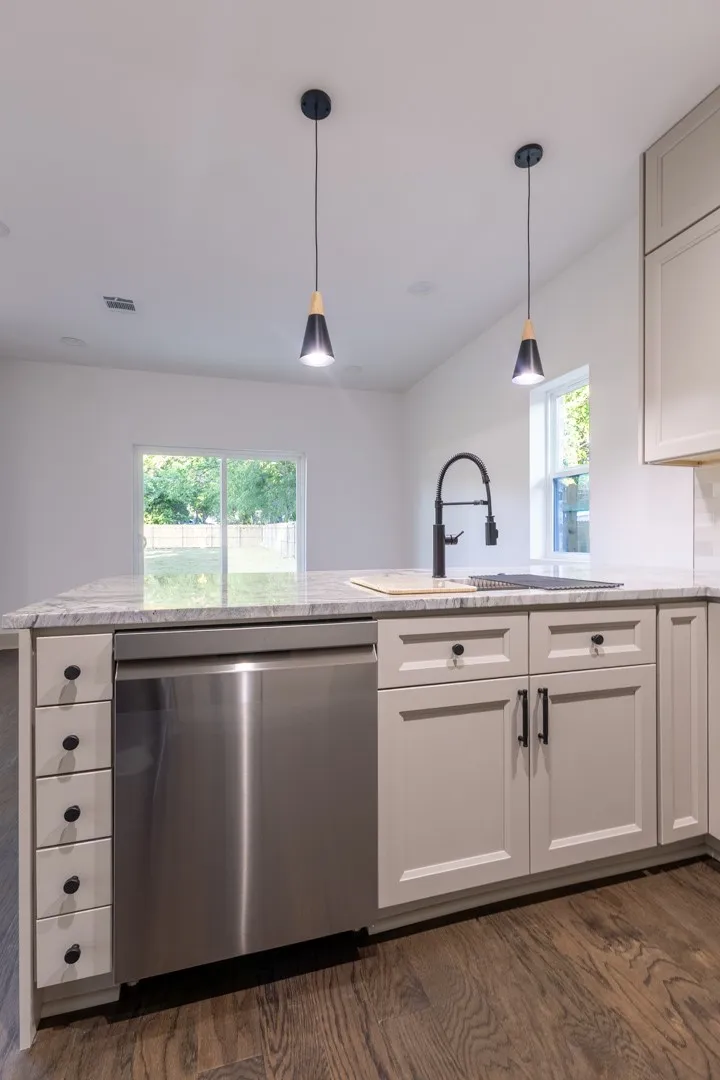 Kitchen island featuring a stainless steel dishwasher, light-toned cabinetry with dark hardware, a single basin sink with a matte black faucet, and a light-toned countertop