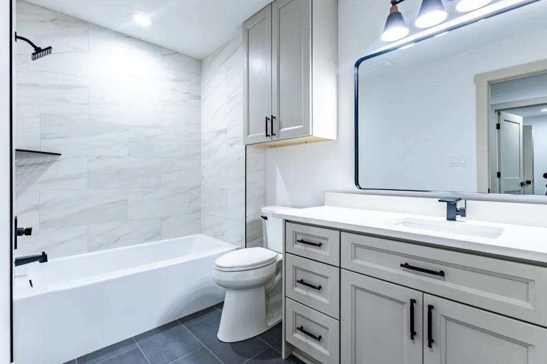 secondary full Bathroom featuring a white subway-tiled tub/shower combination with matte black fixtures, a contemporary vanity with white shaker-style cabinetry, a rectangular undermount sink, and a large framed mirror with overhead lighting