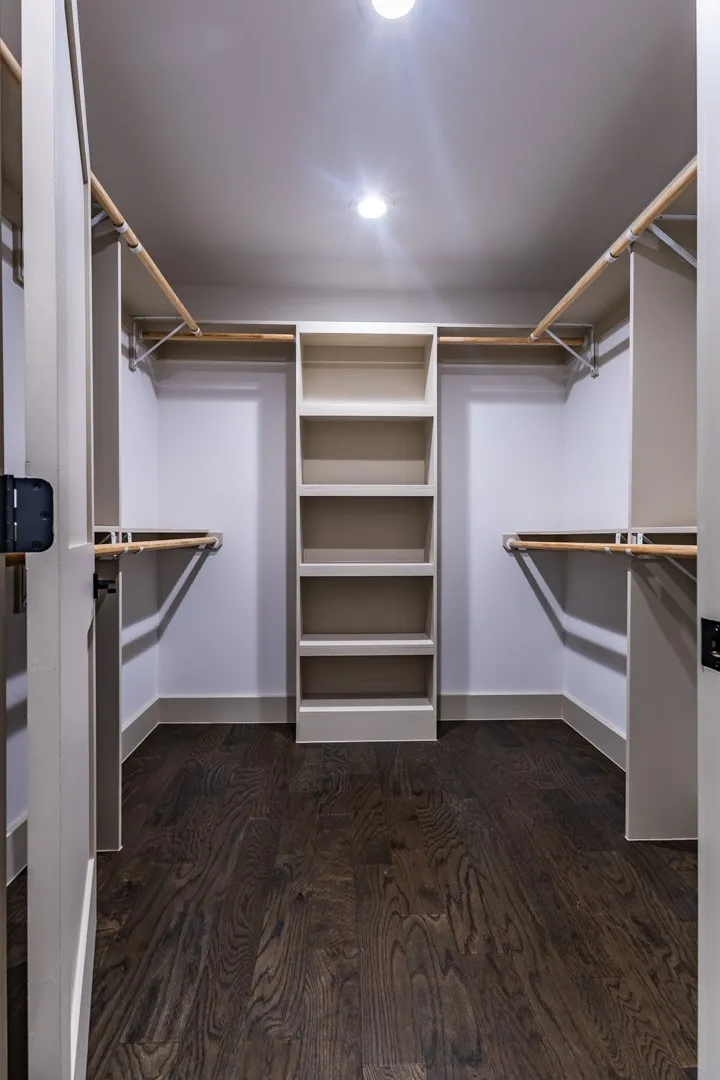 Second primary Walk-in closet featuring built-in shelving, hanging rods, and dark wood-finish flooring