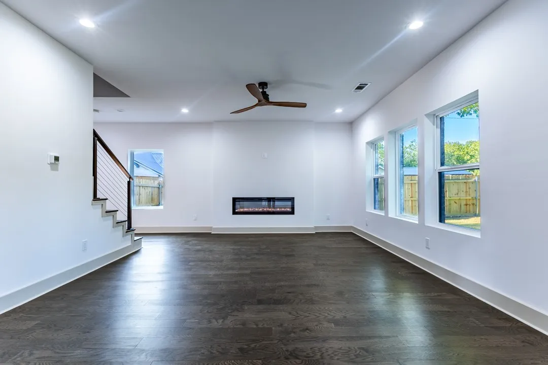 Spacious living area featuring dark wood-finish flooring, a contemporary linear fireplace, and multiple windows