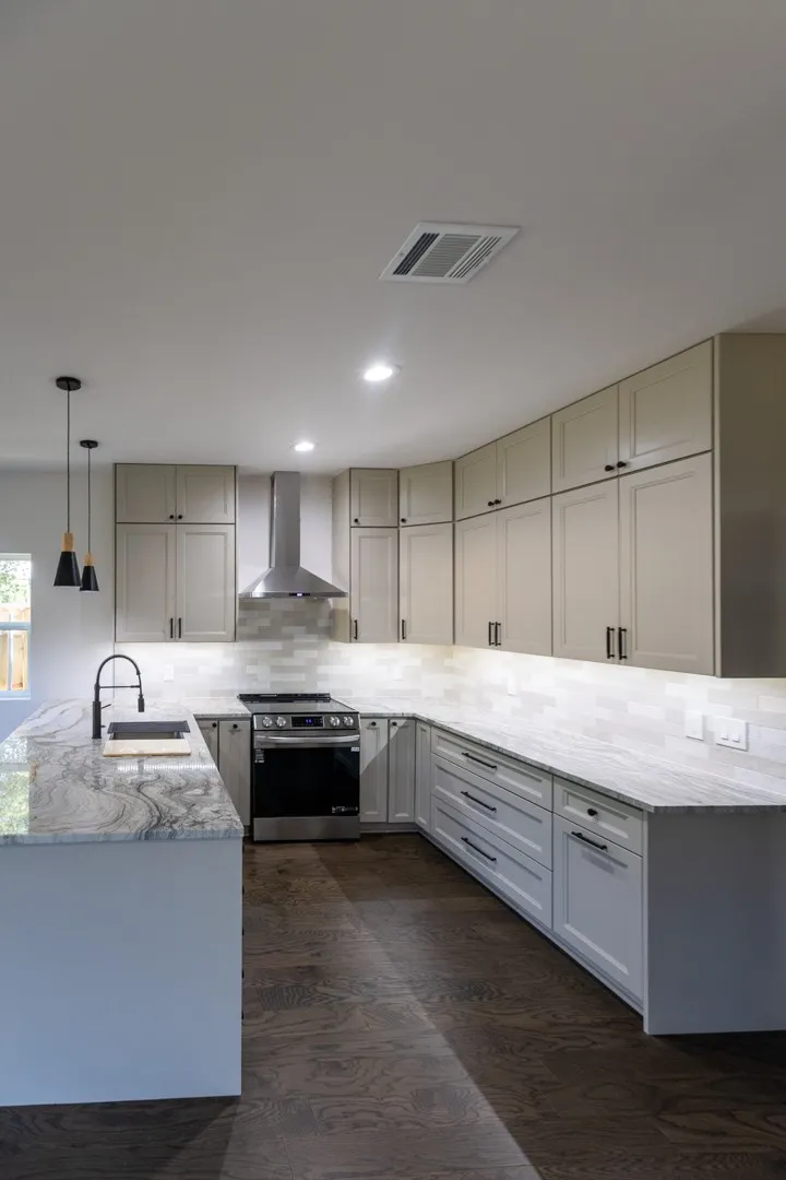 U-shaped kitchen featuring light-toned shaker cabinetry, dark wood-finish flooring, and light-toned countertops with distinctive veining