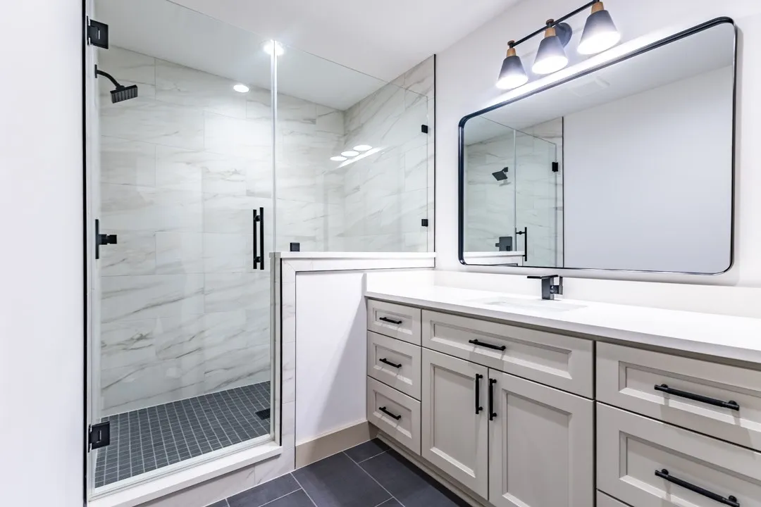 Modern bathroom featuring a frameless glass shower enclosure with rainfall showerhead, white marble-look shower tile, and dark gray mosaic shower floor
