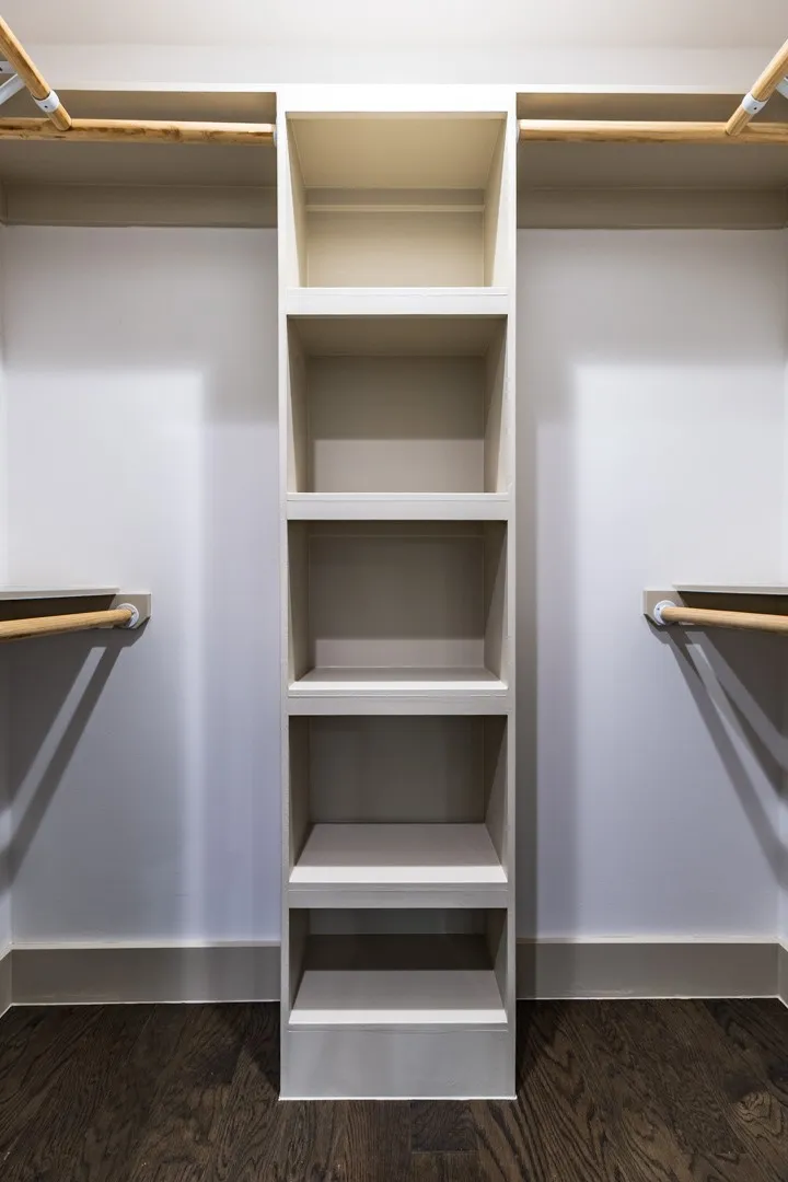 Built-in closet system featuring central shelving units, dual hanging rods, and dark wood-finish flooring