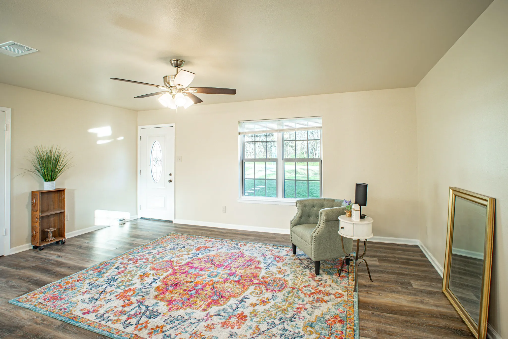 Spacious interior featuring wood-finish flooring, neutral paint, a ceiling fan with light fixture, and a white entry door with an oval glass insert